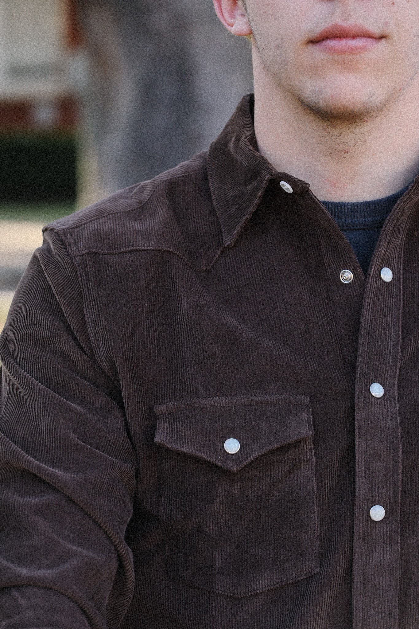 Close-up of a man wearing a brown corduroy jacket with snap buttons and a chest pocket, outdoors