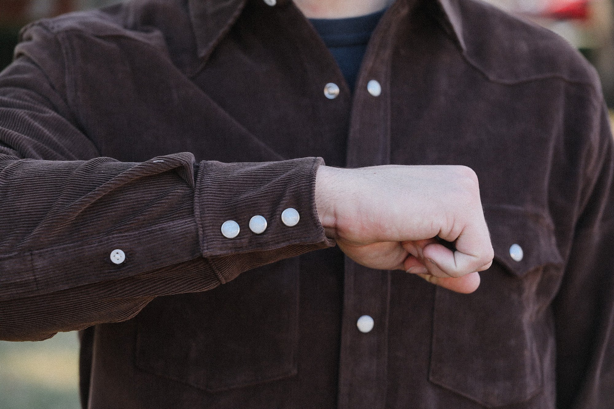 Close-up of a man's arm wearing a brown corduroy shirt with silver snap buttons, set outdoors
