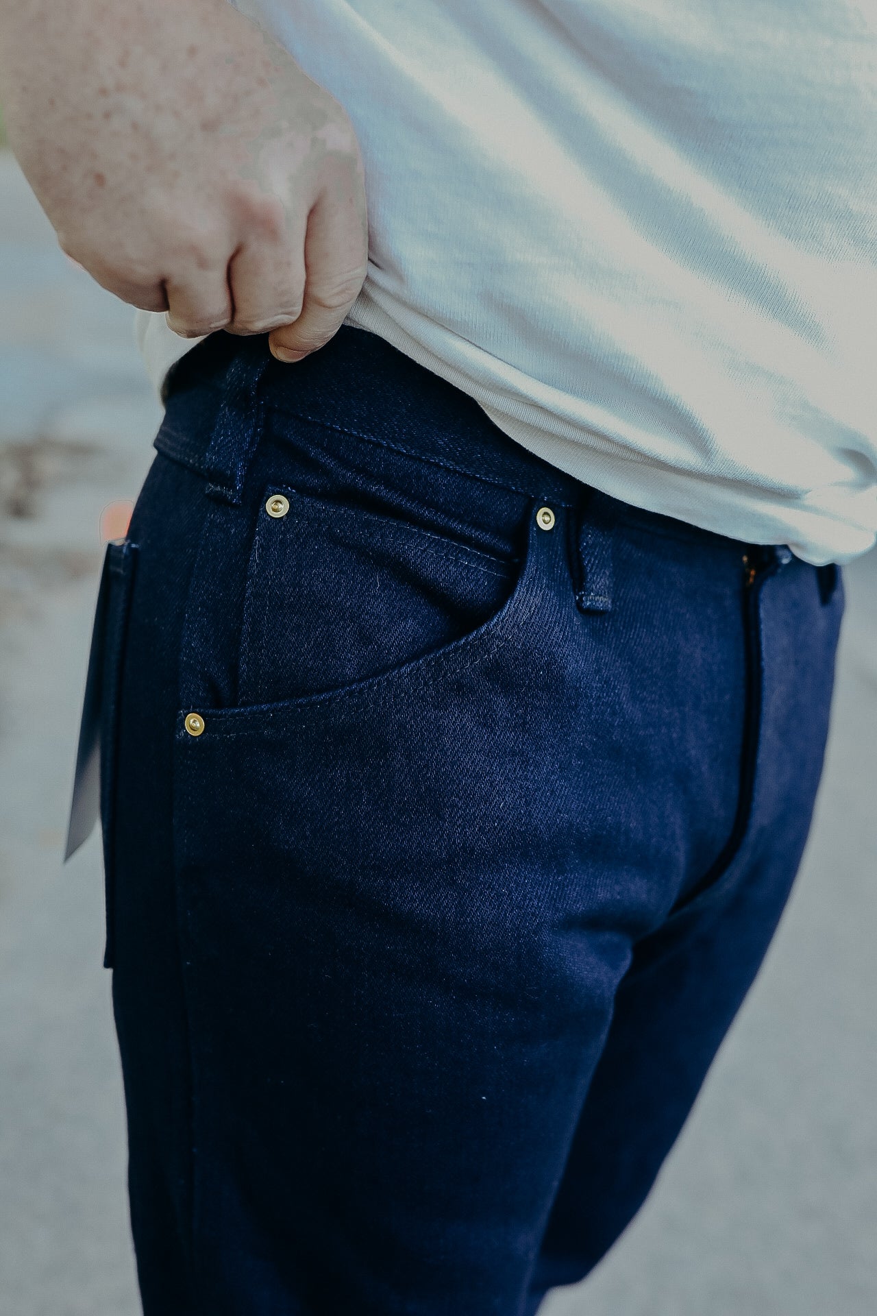 Close-up of person wearing dark blue denim jeans with gold rivets and white t-shirt lifting hem