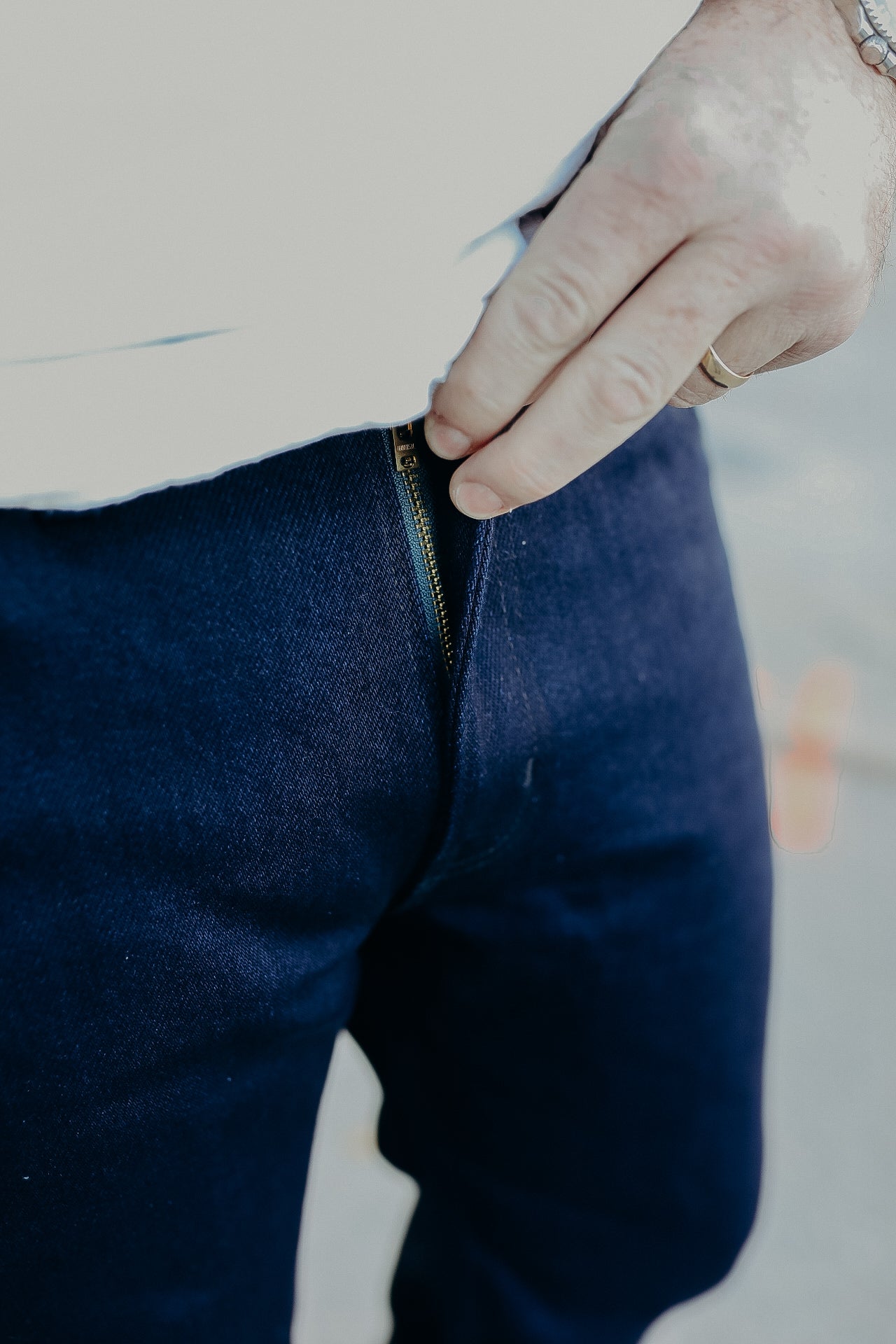 Close-up of hand zipping dark blue denim jeans, showcasing quality zipper detail