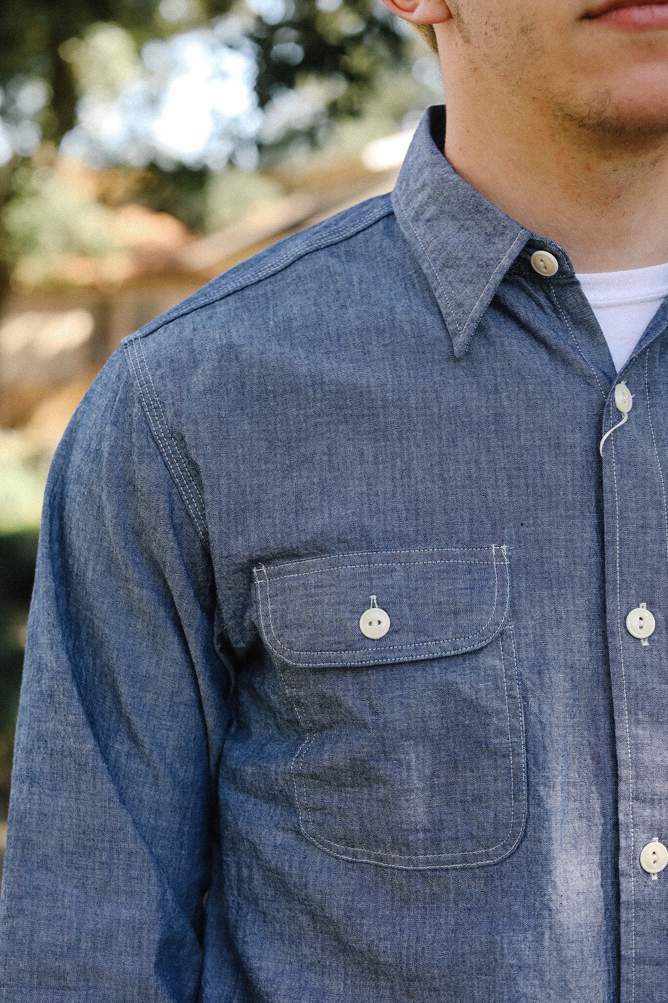 Close-up of man wearing blue chambray work shirt with buttoned chest pocket outdoors