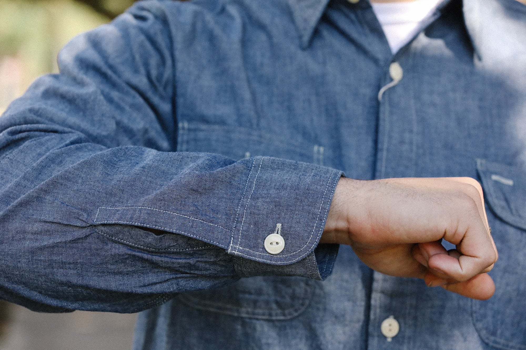 Close-up of a person wearing a blue chambray work shirt with buttoned cuff, showcasing durable fabric detail