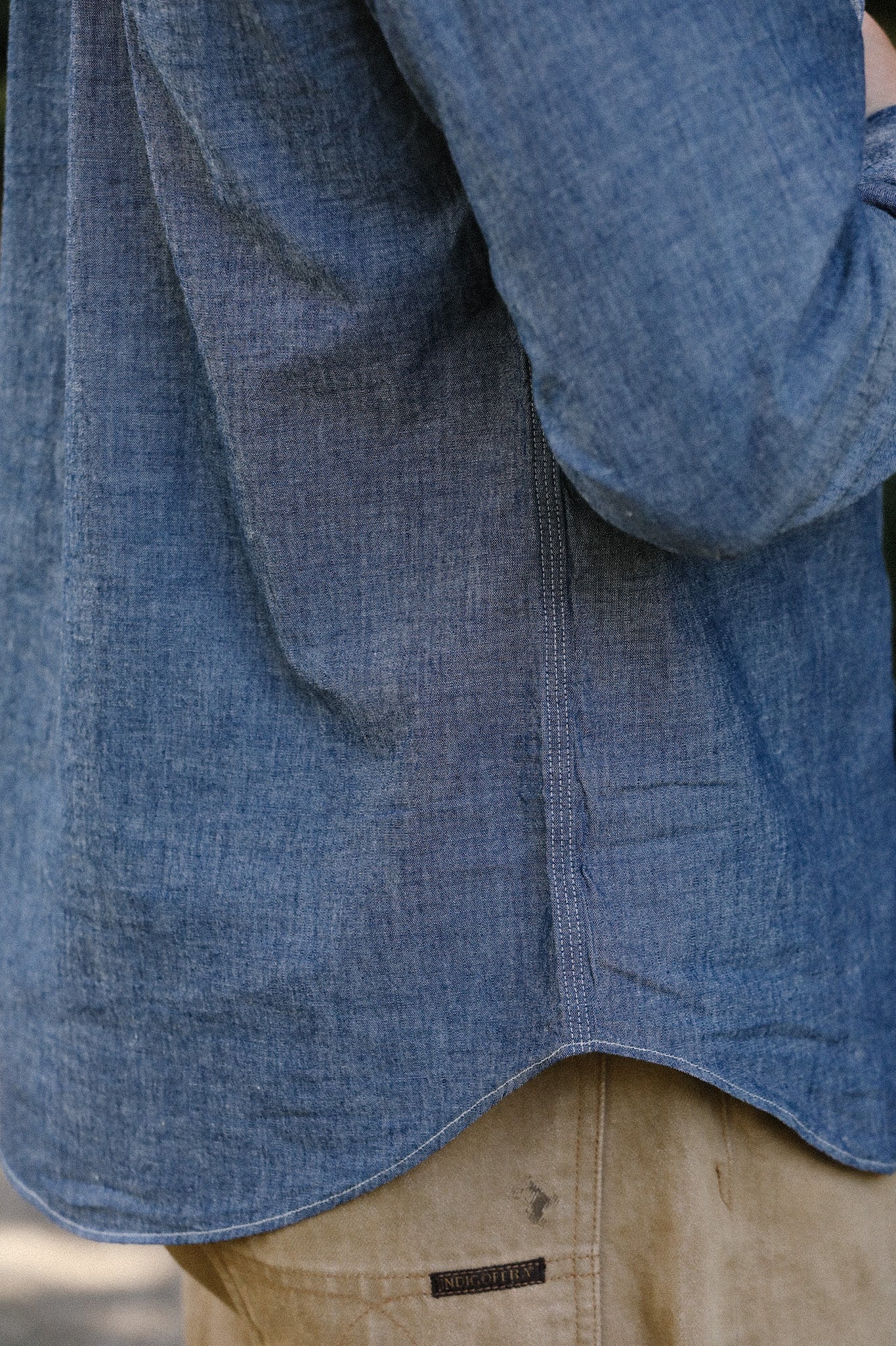 Close-up of denim blue shirt hem over beige pants with indigo label, casual outdoor wear
