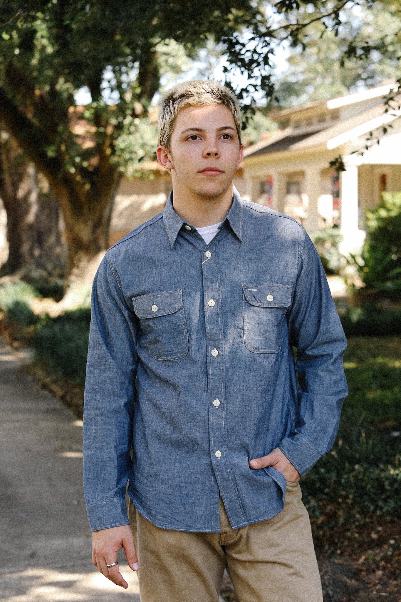 Young man outdoors wearing a blue chambray work shirt and beige pants at Iron Shop Provisions