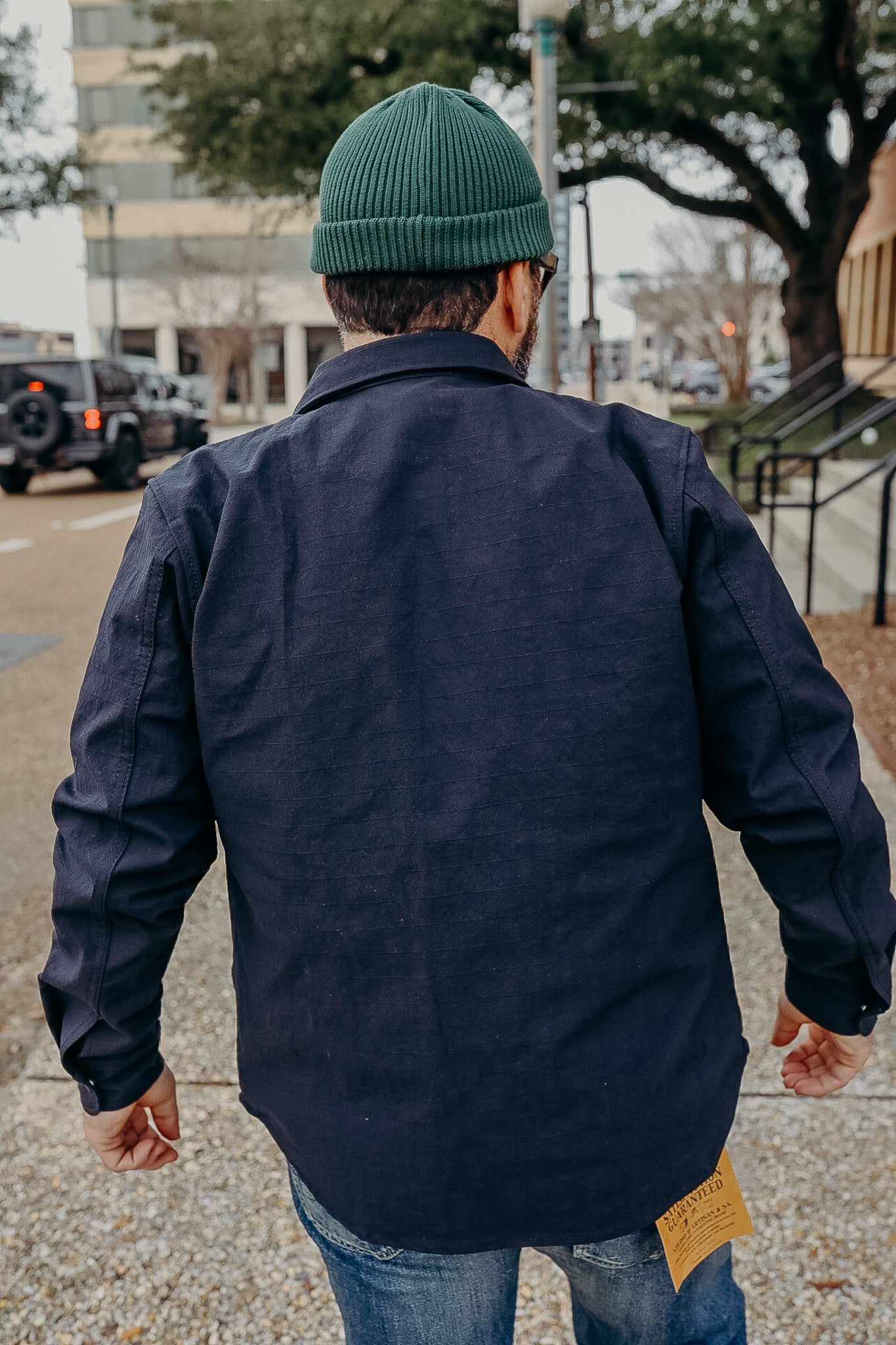 Man wearing a navy blue heavy cotton jacket and green knit beanie, walking on city sidewalk