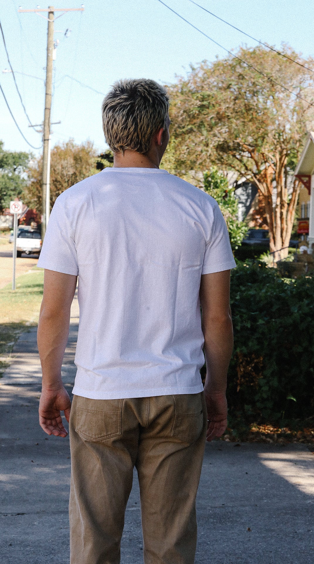 Man with short hair wearing a plain white t-shirt and khaki pants standing outdoors on a sidewalk