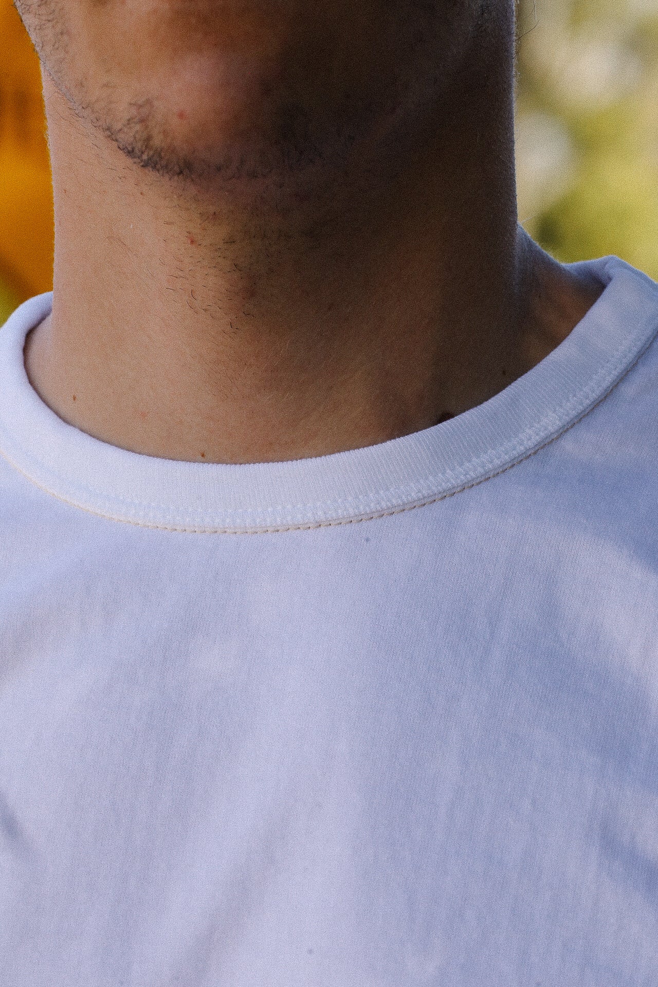 Close-up of male neck and chin wearing a white crew neck t-shirt outdoors