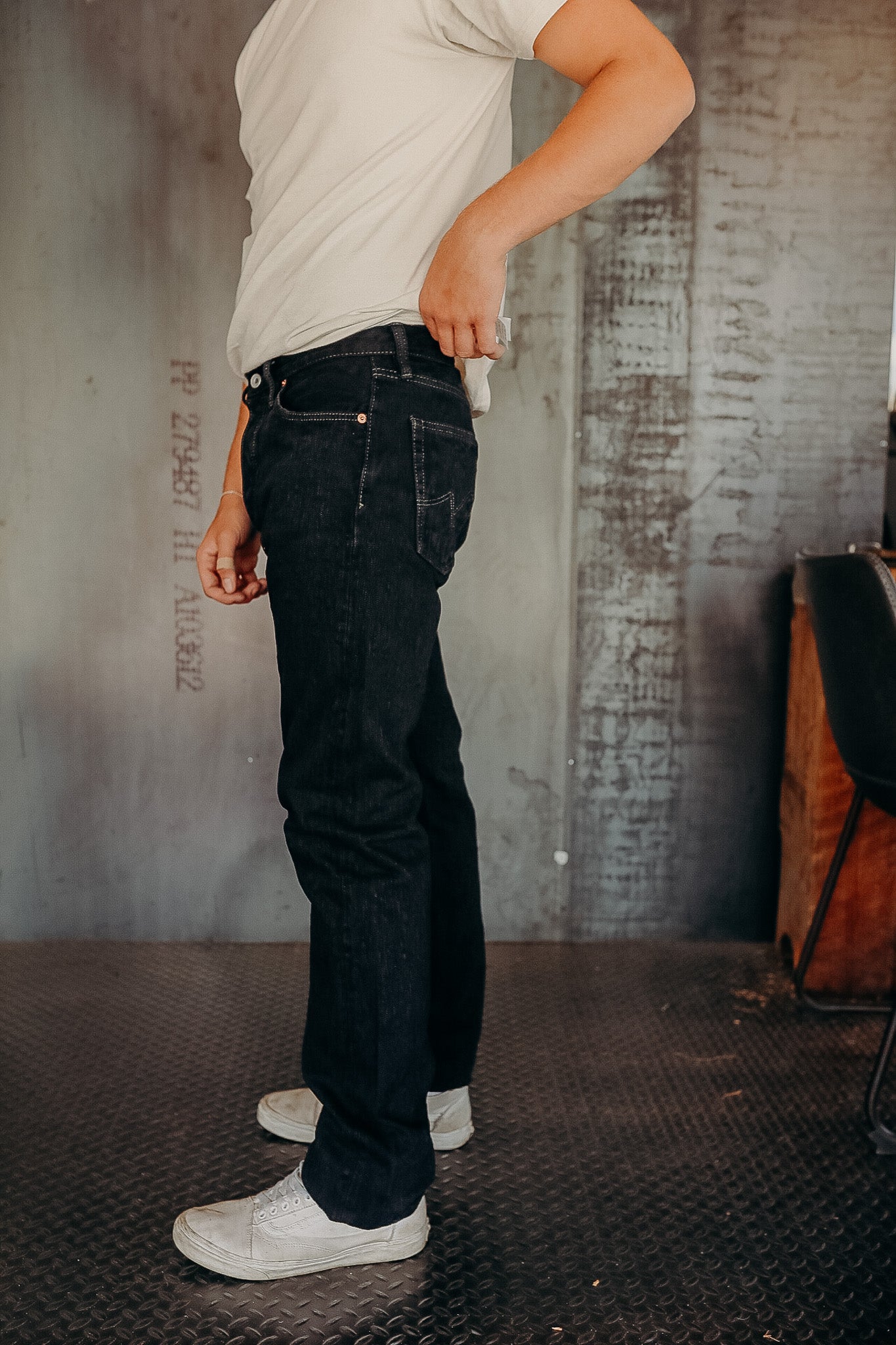 Person wearing black denim jeans and white sneakers standing on industrial metal floor