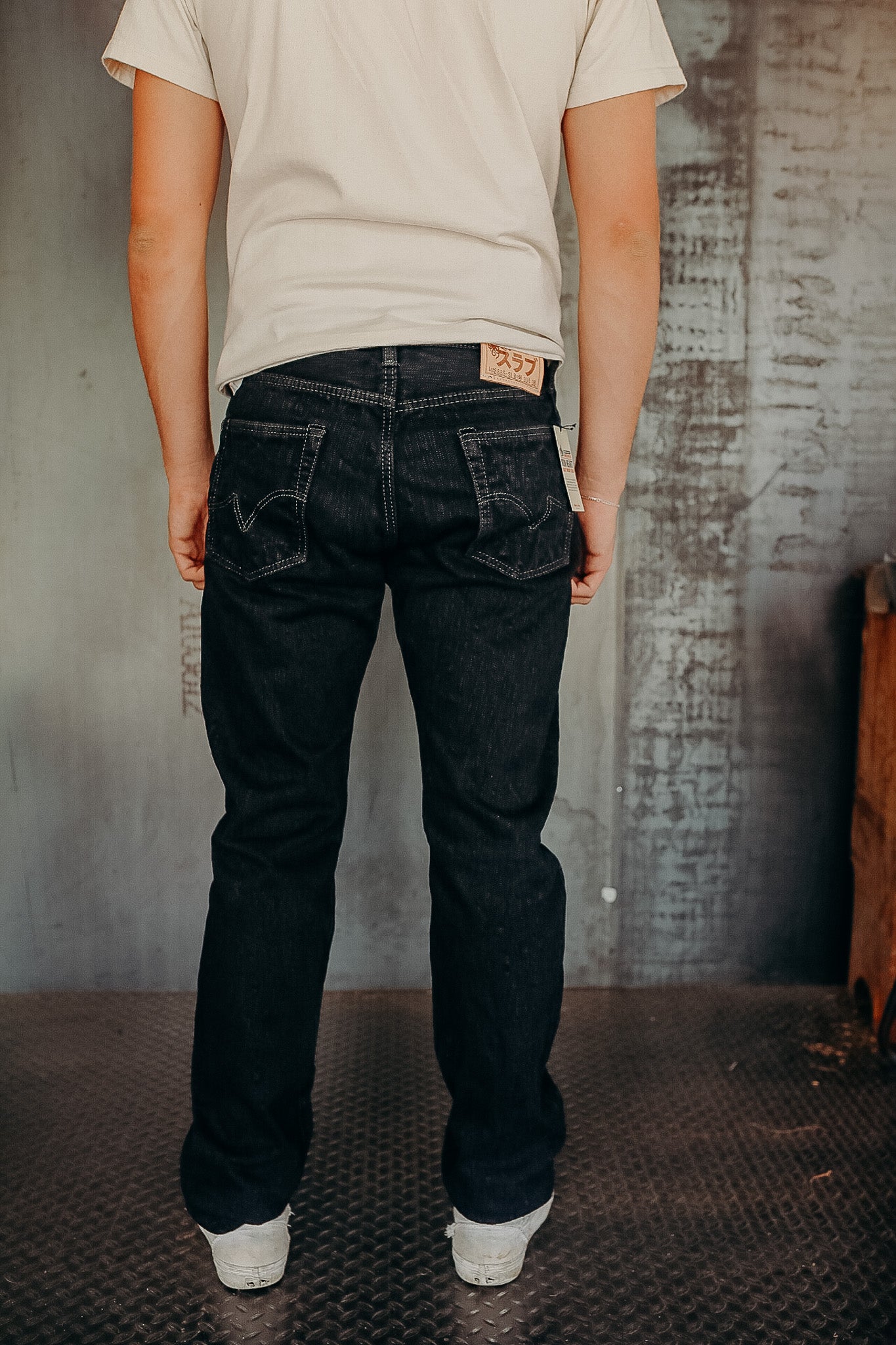 Back view of person wearing black denim jeans and white sneakers in industrial interior