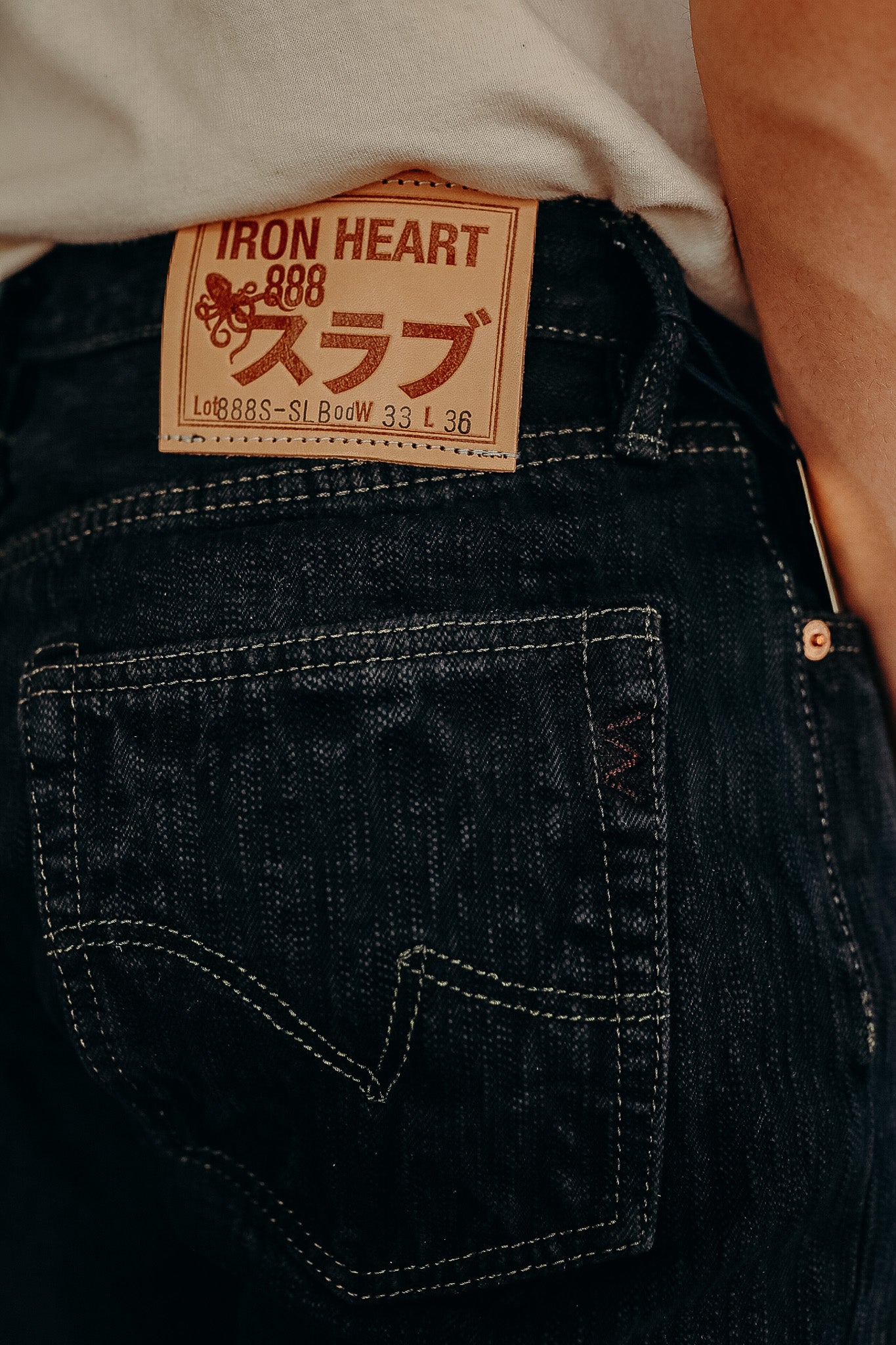 Close-up of Iron Heart 888 dark denim jeans showing leather brand patch and pocket stitching