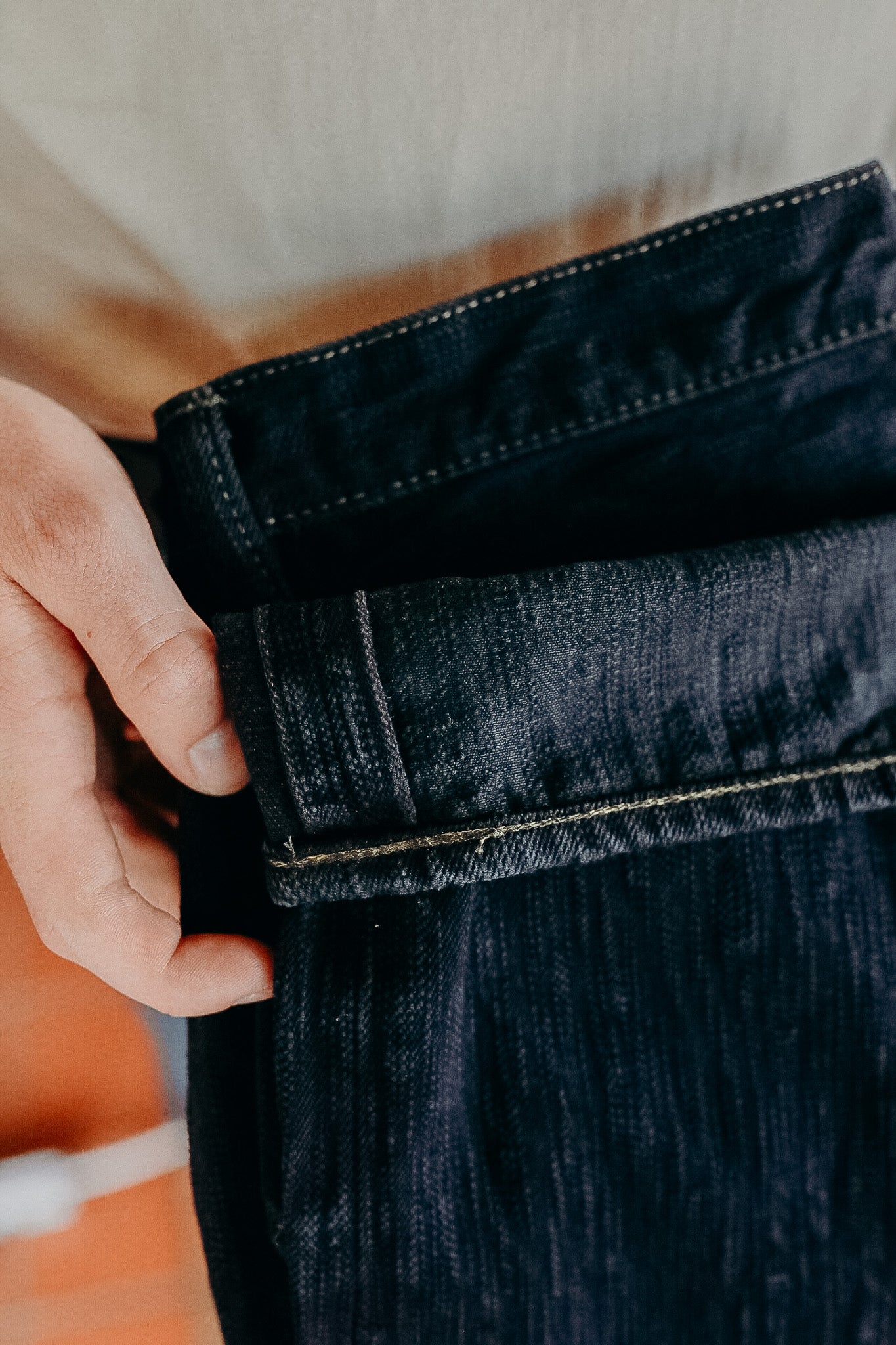 Close-up of hand holding dark denim jeans cuff with visible stitching at Iron Shop Provisions