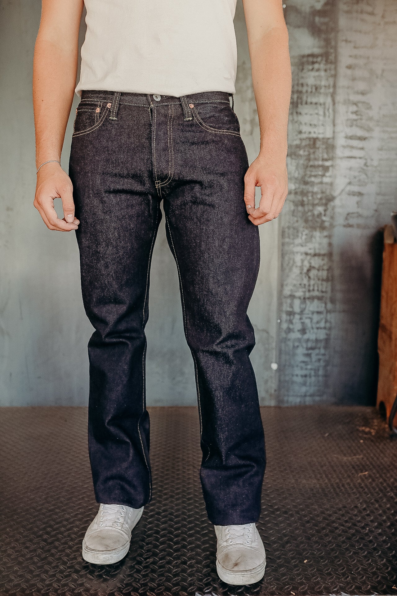 Man wearing dark raw denim jeans and white sneakers standing on textured metal floor
