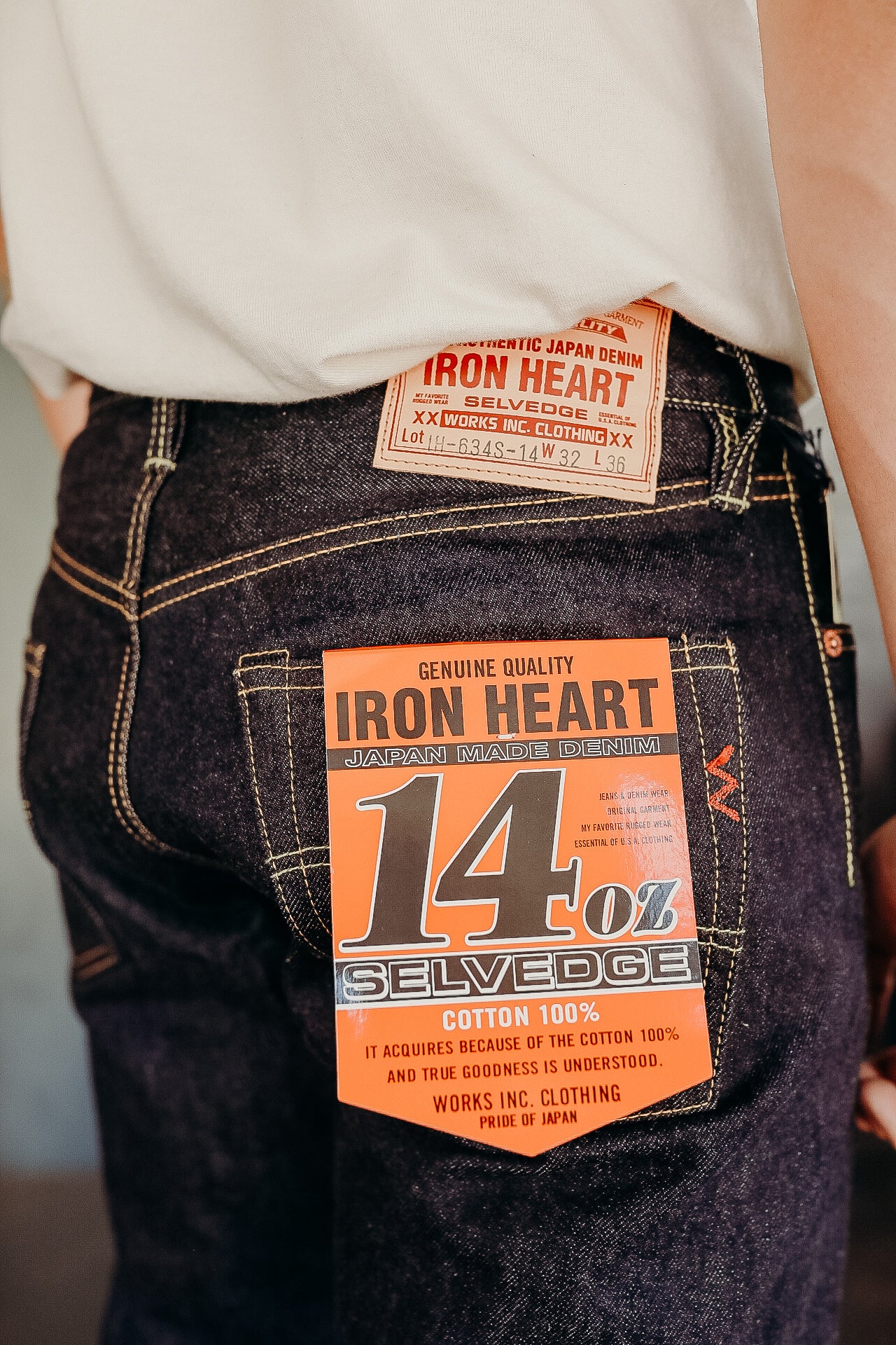 Close-up of person wearing Iron Heart Japan made 14oz selvedge denim jeans with orange label on back pocket