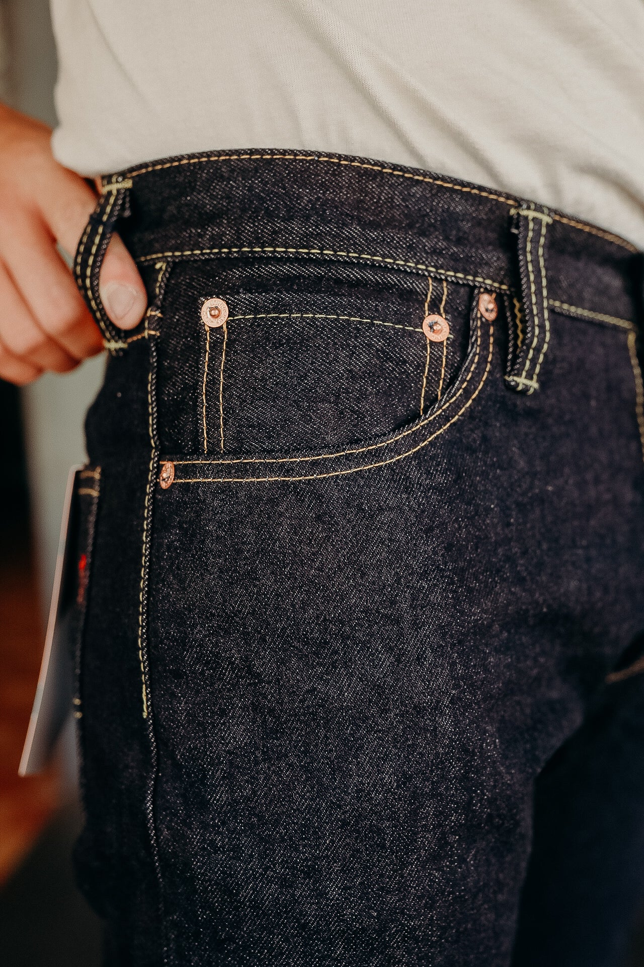 Close-up of dark raw denim jeans with yellow stitching and copper rivets from Iron Shop Provisions