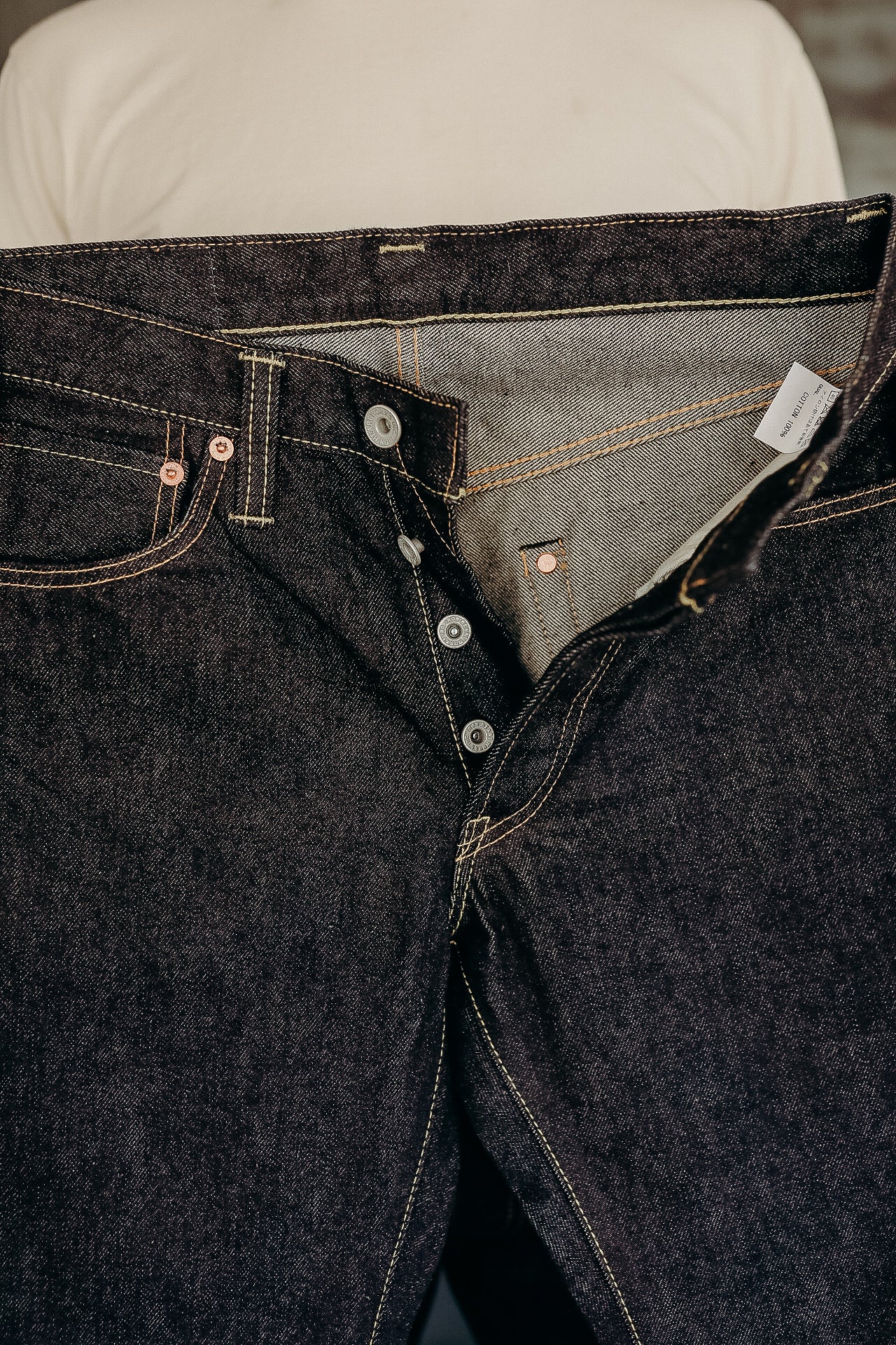 Close-up of dark raw denim jeans with button fly and visible stitching details