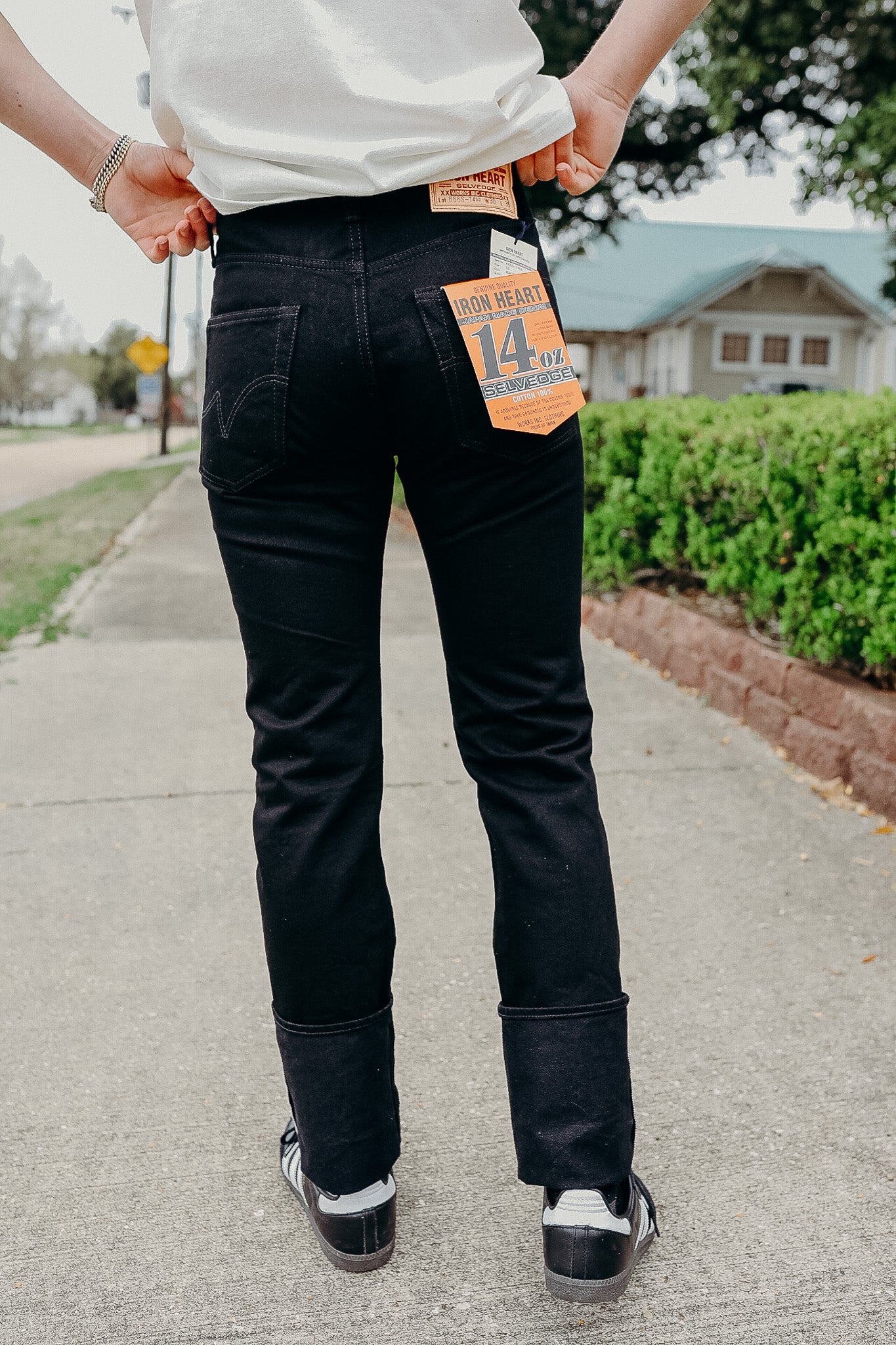 Person wearing black Iron Heart 14oz selvedge denim jeans with labels outdoors on sidewalk