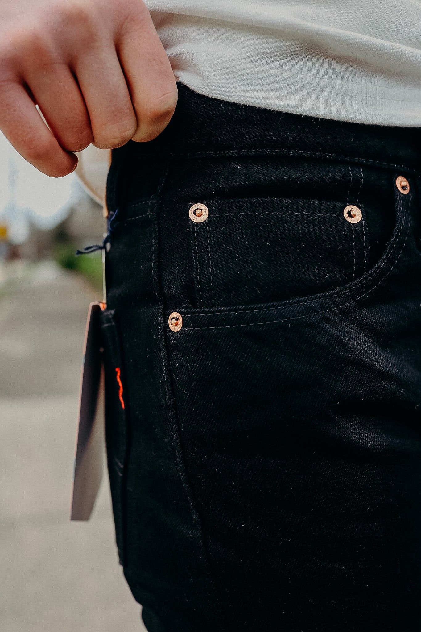 Close-up of black denim jeans pocket with copper rivets and a hand resting on the waistband