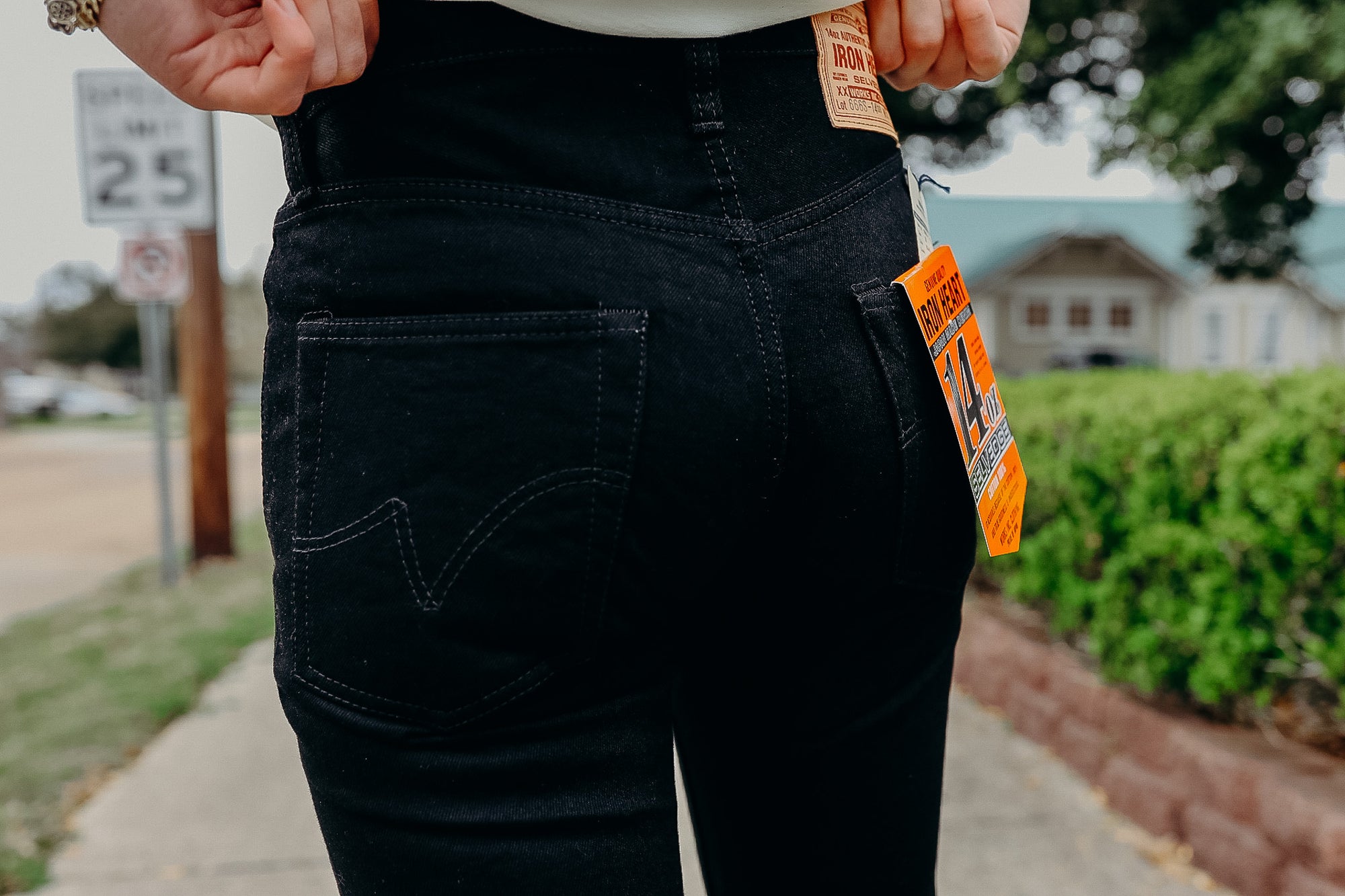 Close-up of person wearing black Iron Heart 14 oz Selvage denim jeans with visible brand tags outdoors