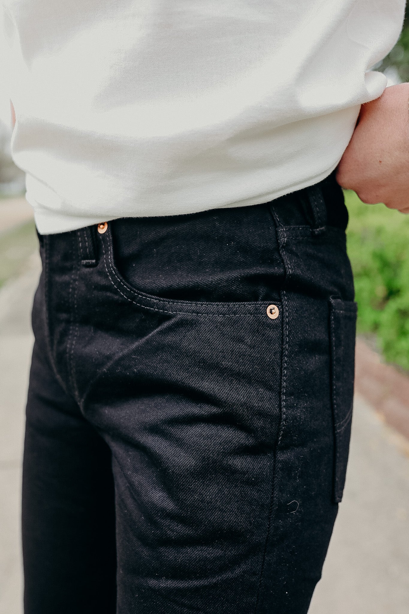 Close-up of person wearing black denim jeans and white shirt outdoors, showcasing pocket and stitching details
