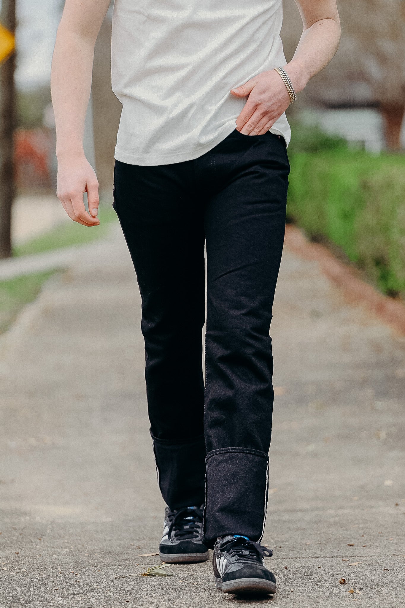 Person wearing black pants with reinforced lower leg panels and black sneakers walking outdoors