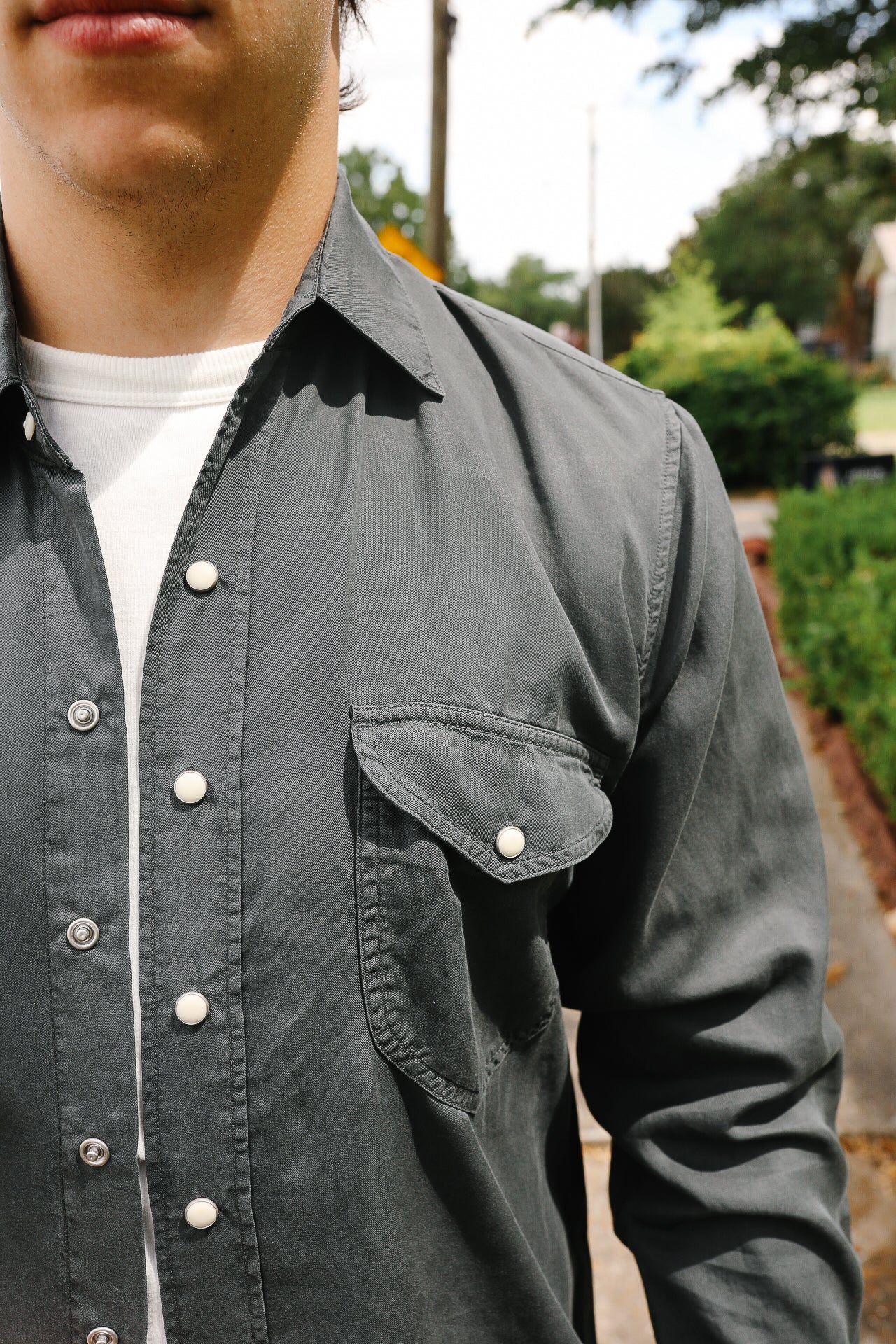 Close-up of a man wearing a dark gray button-up shirt with snap buttons and a chest pocket outdoors