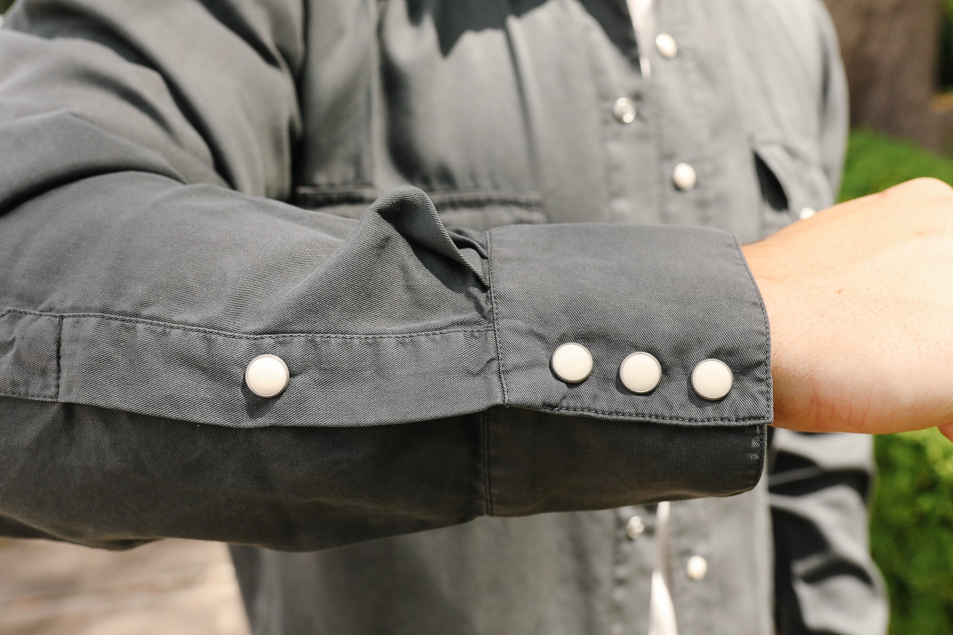 Close-up of a charcoal gray work shirt sleeve with white snap buttons from Iron Shop Provisions