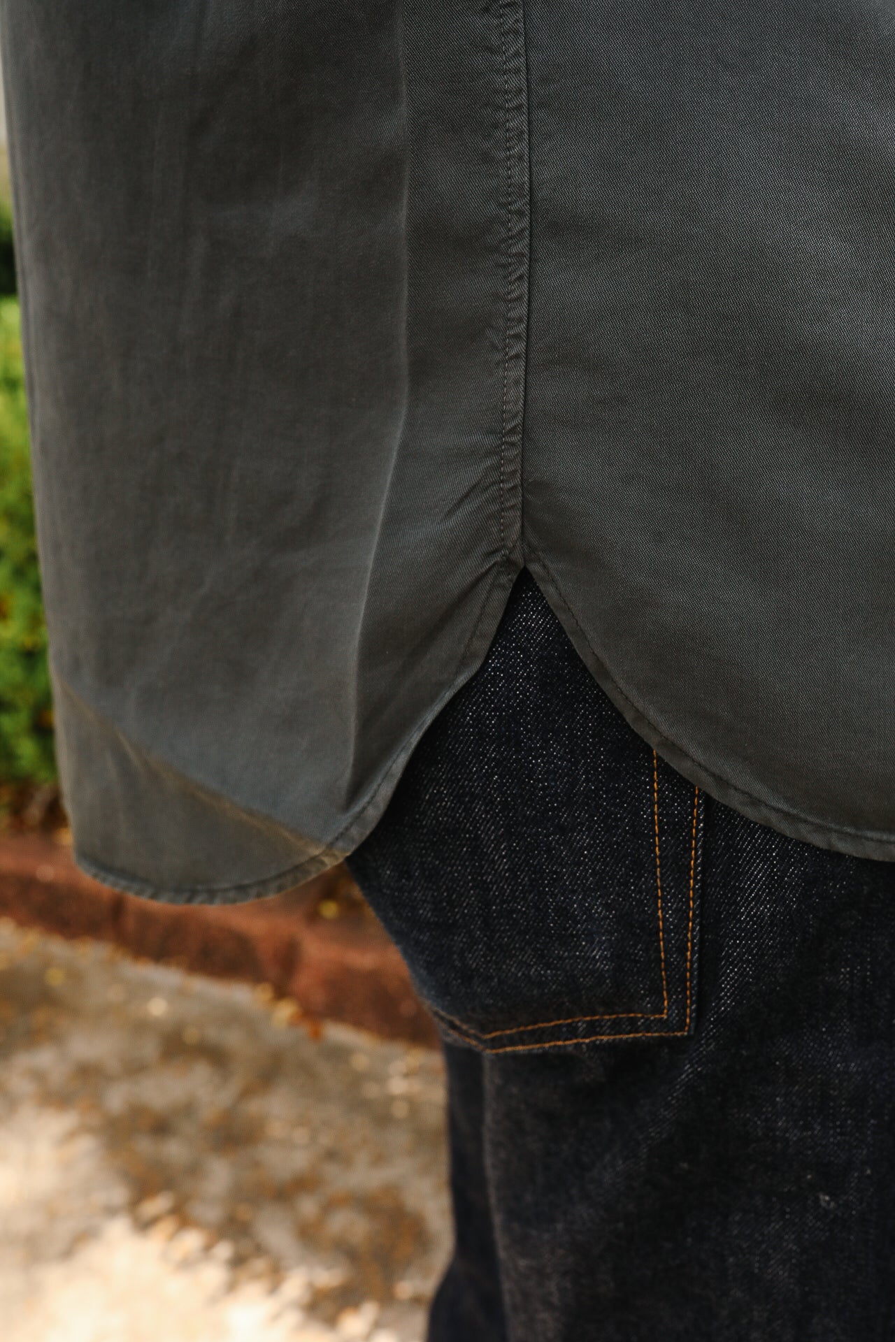 Close-up of dark gray shirt hem with side slit over dark denim jeans with orange stitching, outdoor setting
