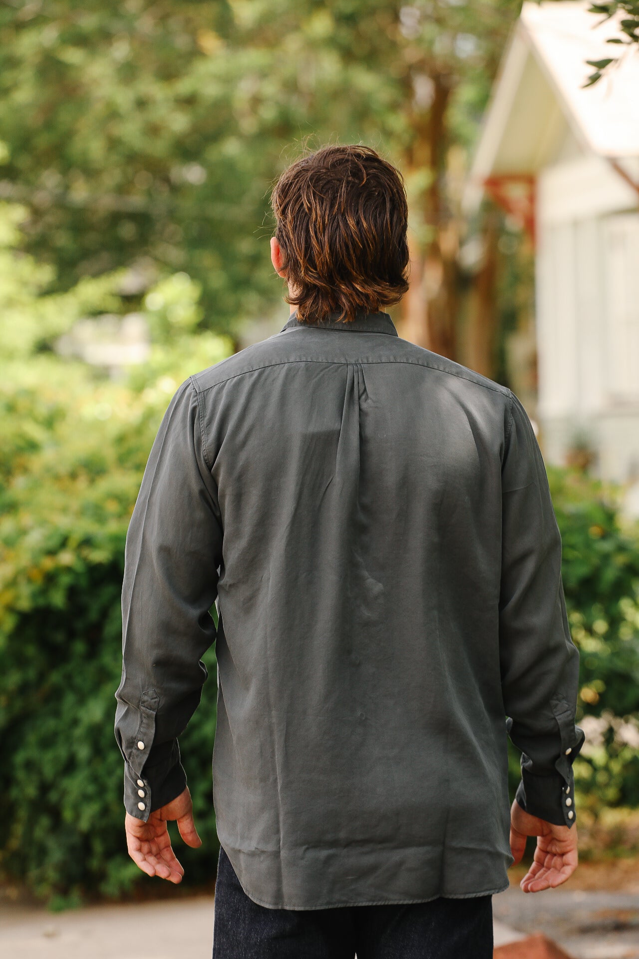 Man wearing a long-sleeve dark gray shirt with snap button cuffs standing outdoors facing away