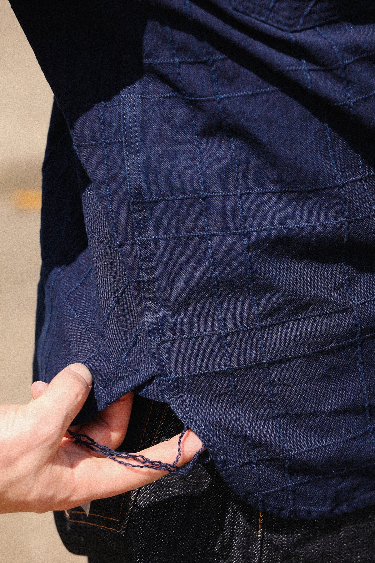 Close-up of a person wearing a dark navy quilted jacket or overshirt with a hand pulling the hem slightly to show the stitching and lining.
