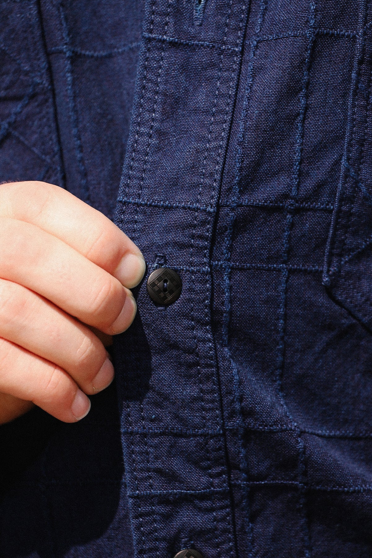 Close-up of a person's hand pulling a dark button on a navy blue quilted button-up shirt.