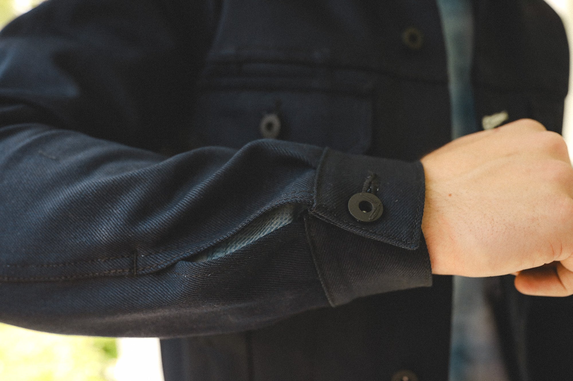 Close-up of a person wearing a dark blue buttoned cuff shirt jacket from Iron Shop Provisions