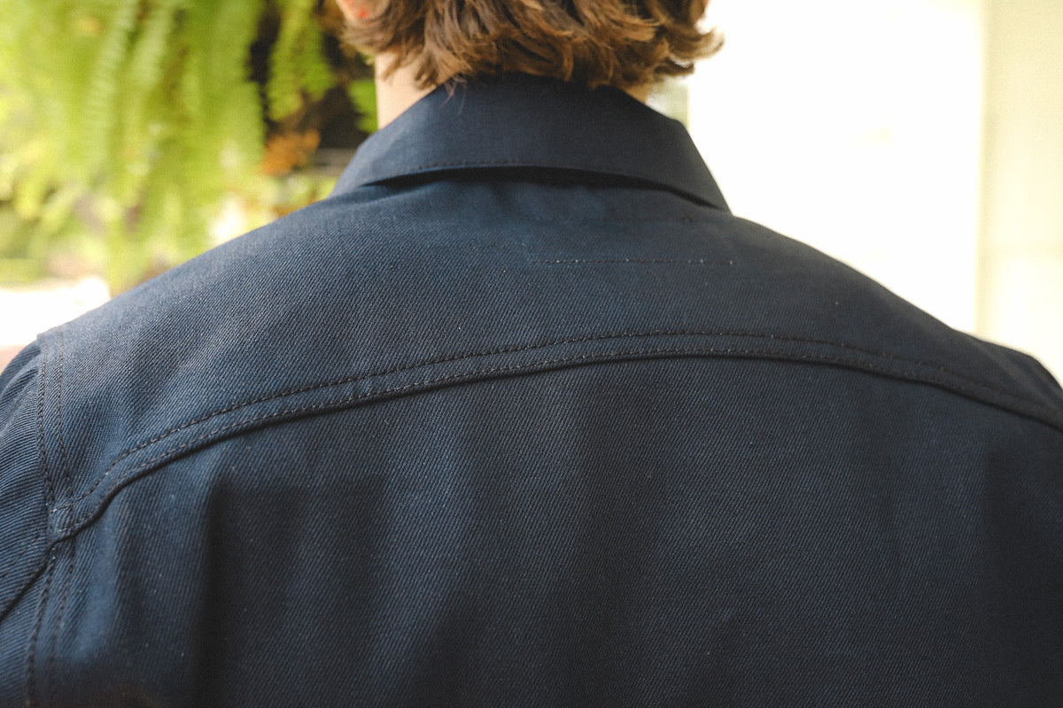 Close-up of person wearing dark navy work shirt with collar and reinforced stitching from behind
