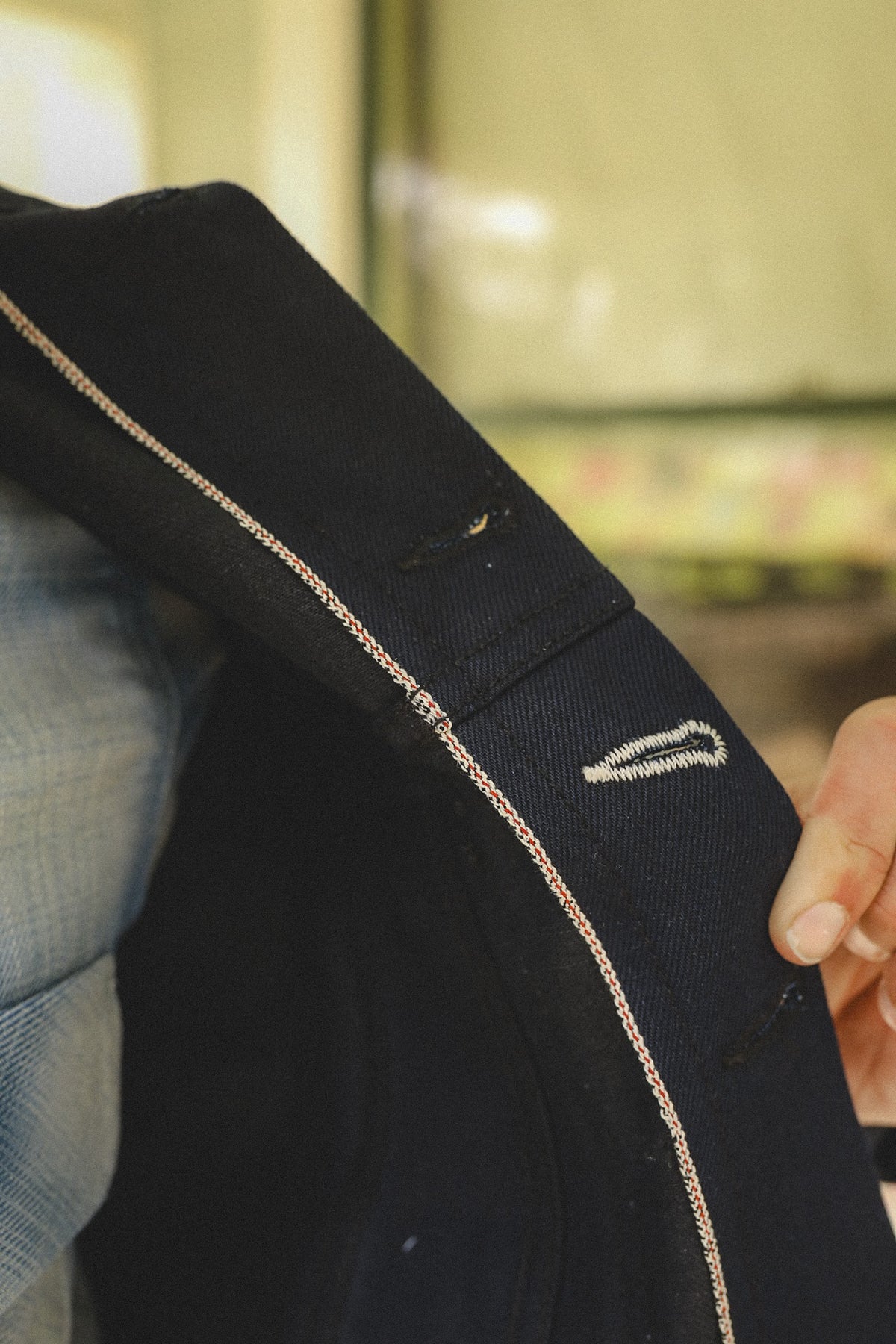 Close-up of black selvedge denim jacket showing edge stitching and buttonholes, held by hand