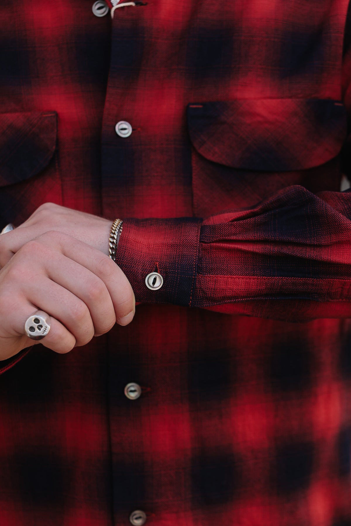 Close-up of a person wearing a red and black plaid flannel button-up shirt, with both hands visible near the cuff and chest pocket area.