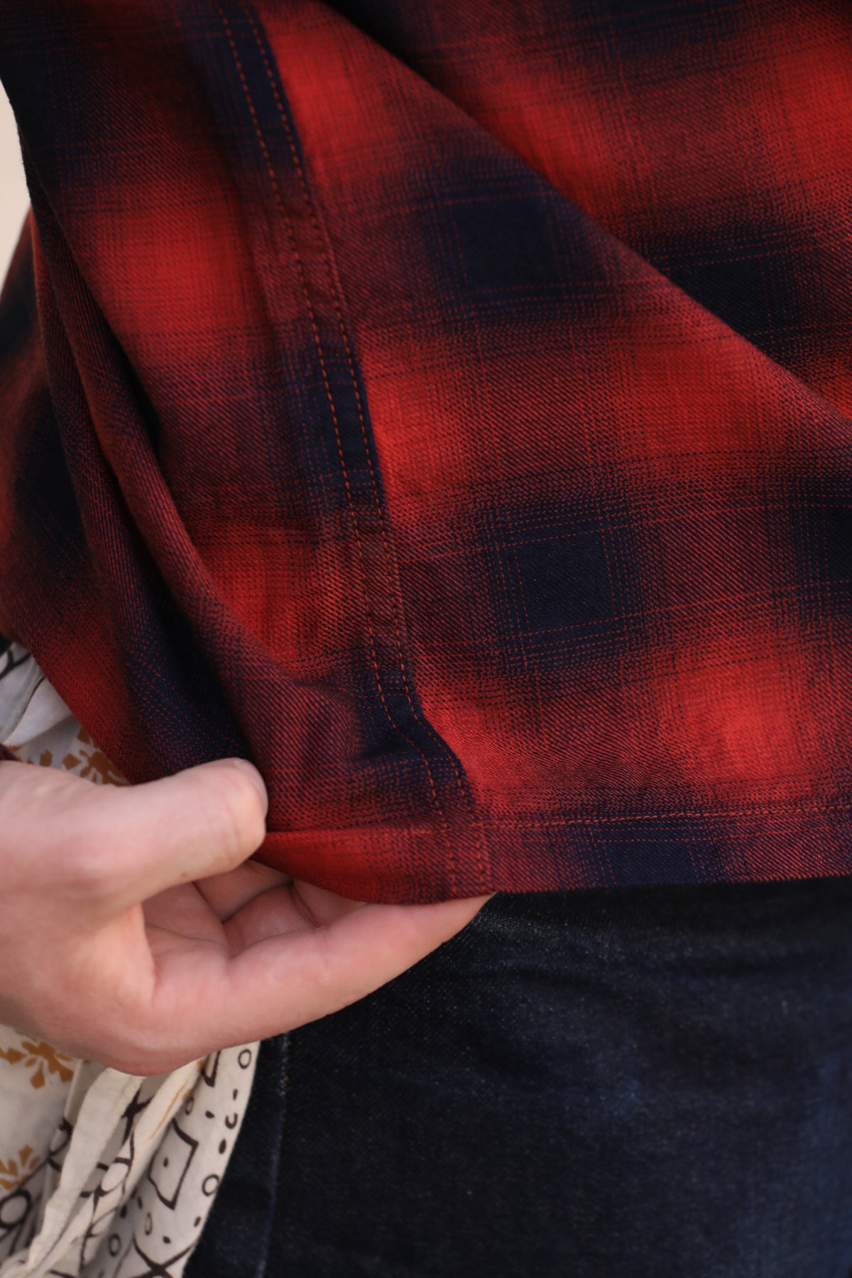 A close-up of a red and black plaid flannel shirt being held by a hand, showing the fabric texture and stitching.