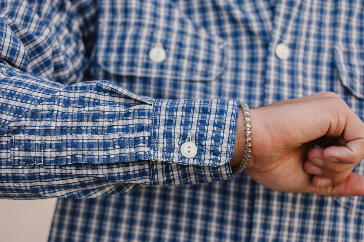 Close-up of a person's wrist wearing a silver beaded bracelet, showing the cuff of a blue and white plaid button-down shirt.