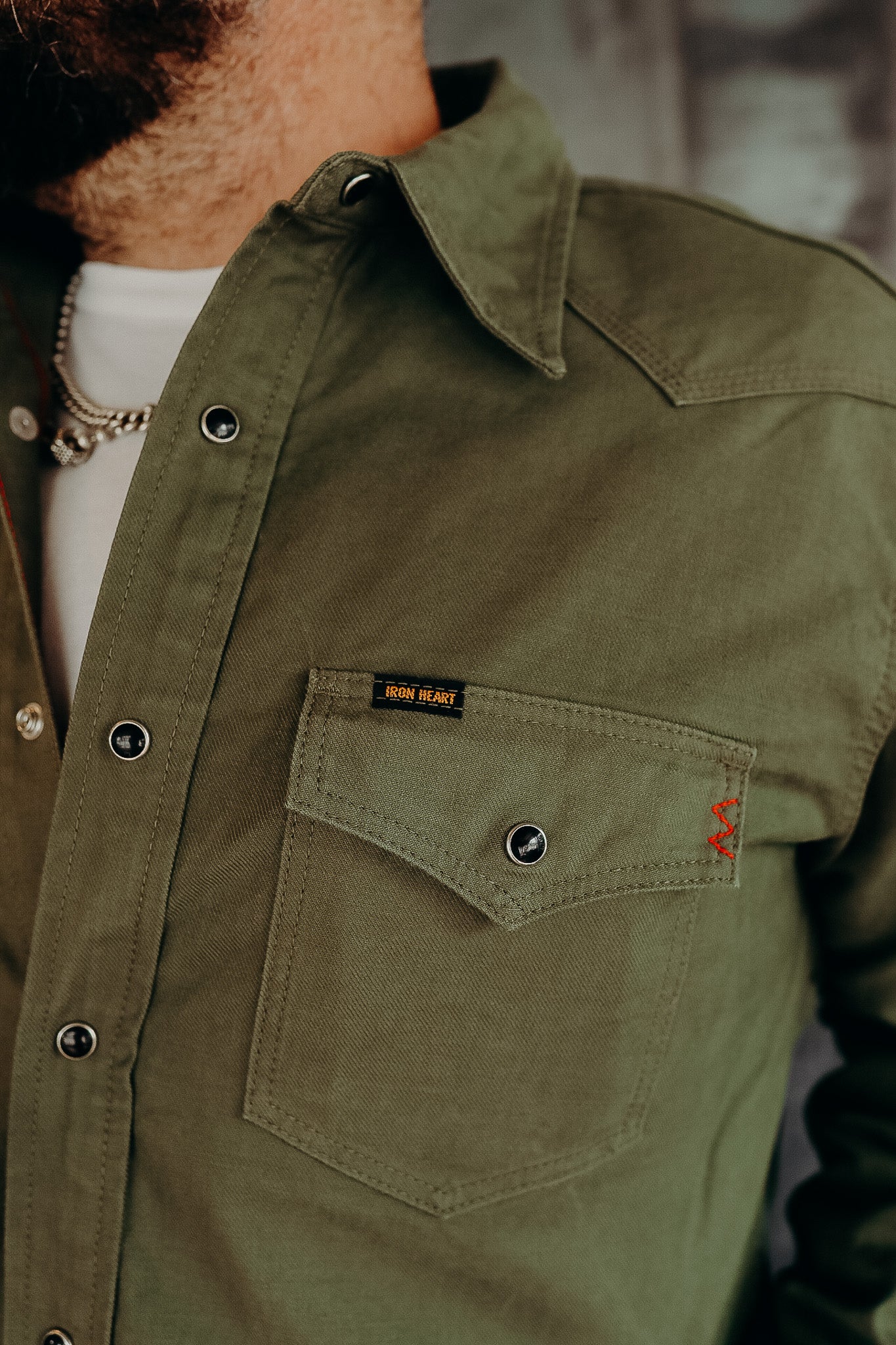 Close-up of man wearing olive green Iron Heart work shirt with chest pocket and snap buttons