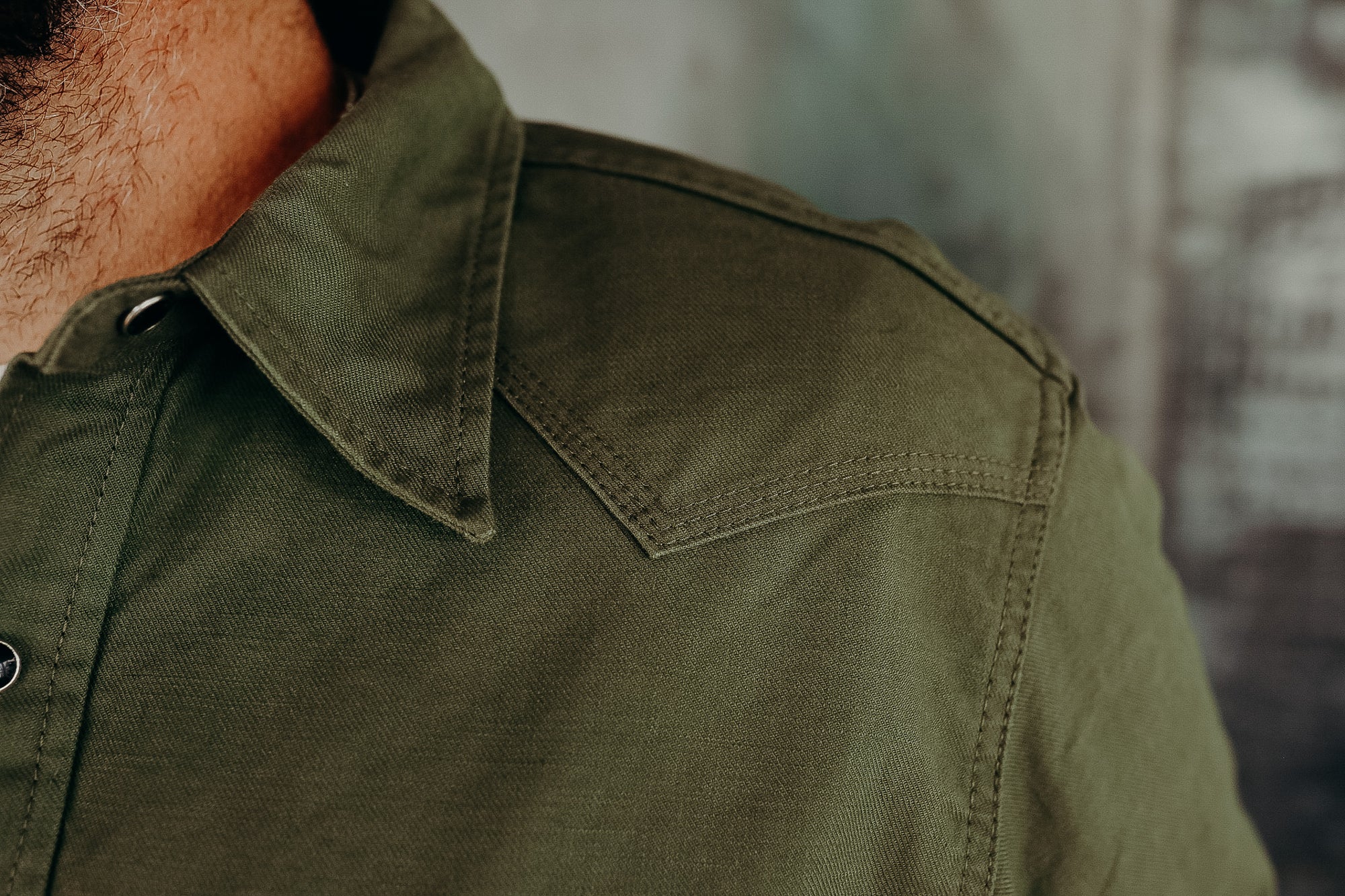 Close-up of a man's neck and olive green denim shirt with detailed stitching on shoulder and collar