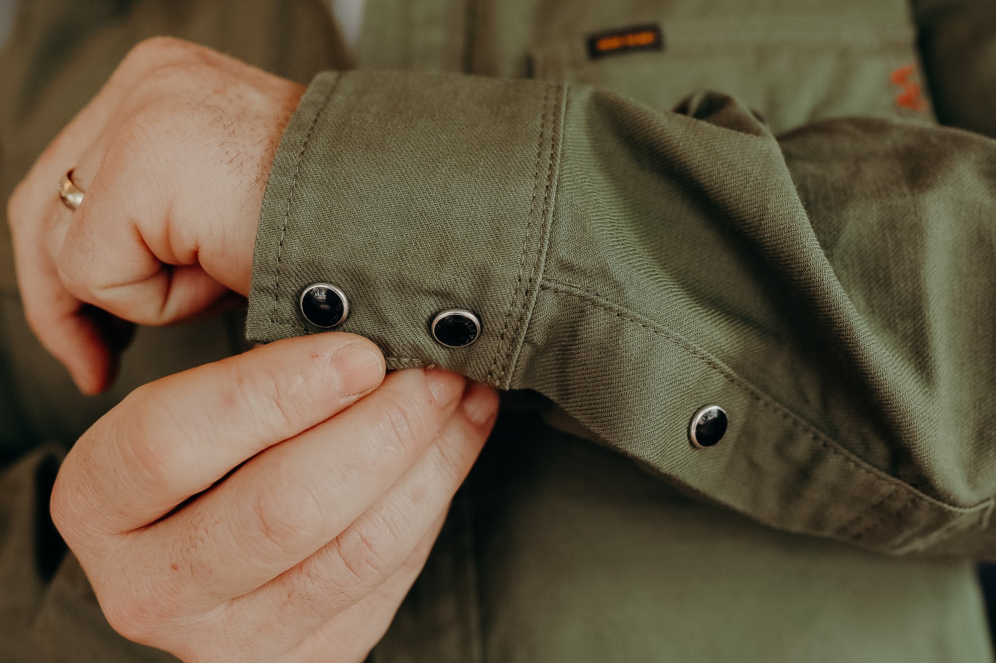 Close-up of a person fastening black snap buttons on an olive green durable shirt cuff