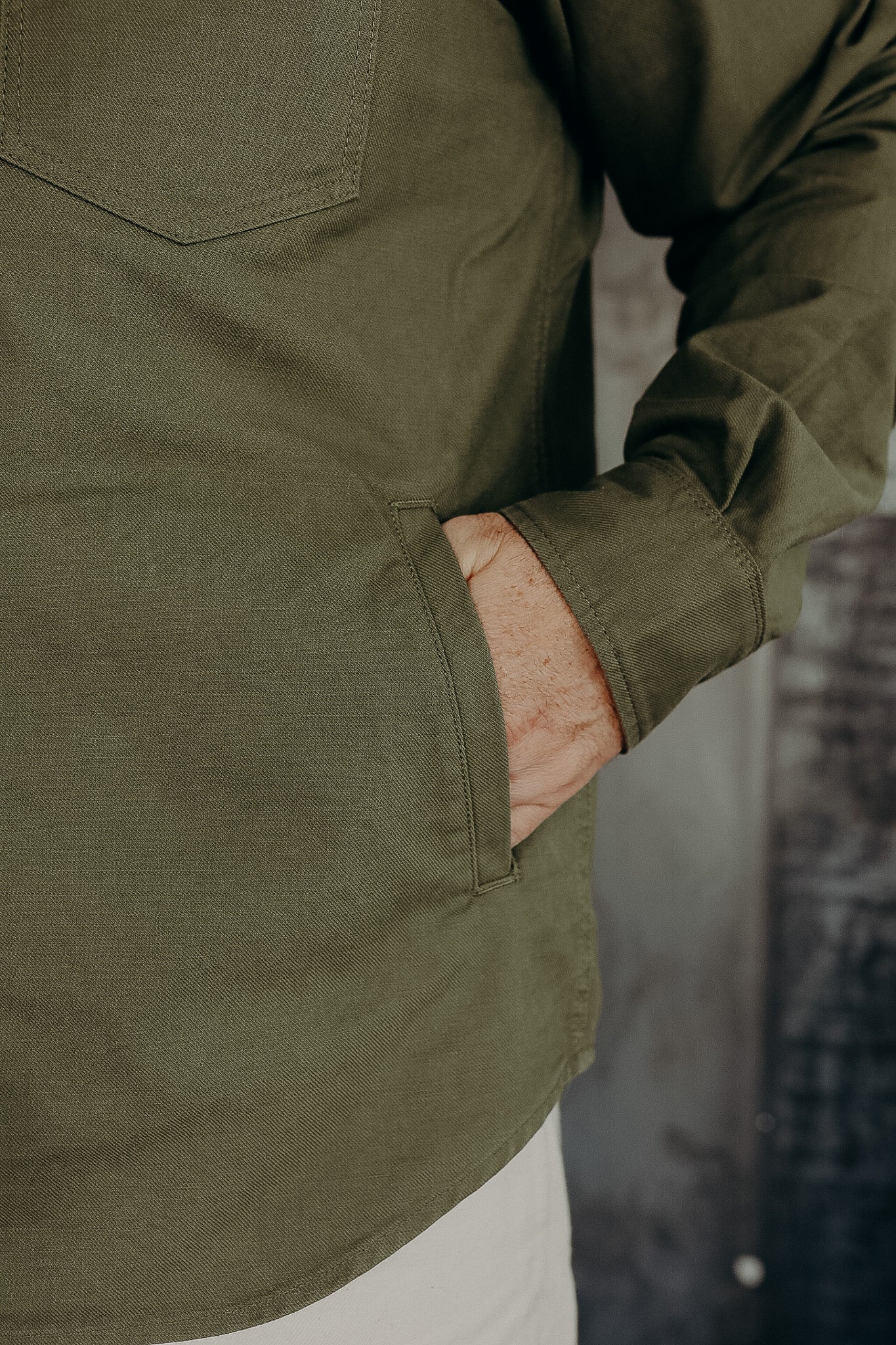 Close-up of a person wearing an olive green long-sleeve shirt with hand in side pocket, casual style