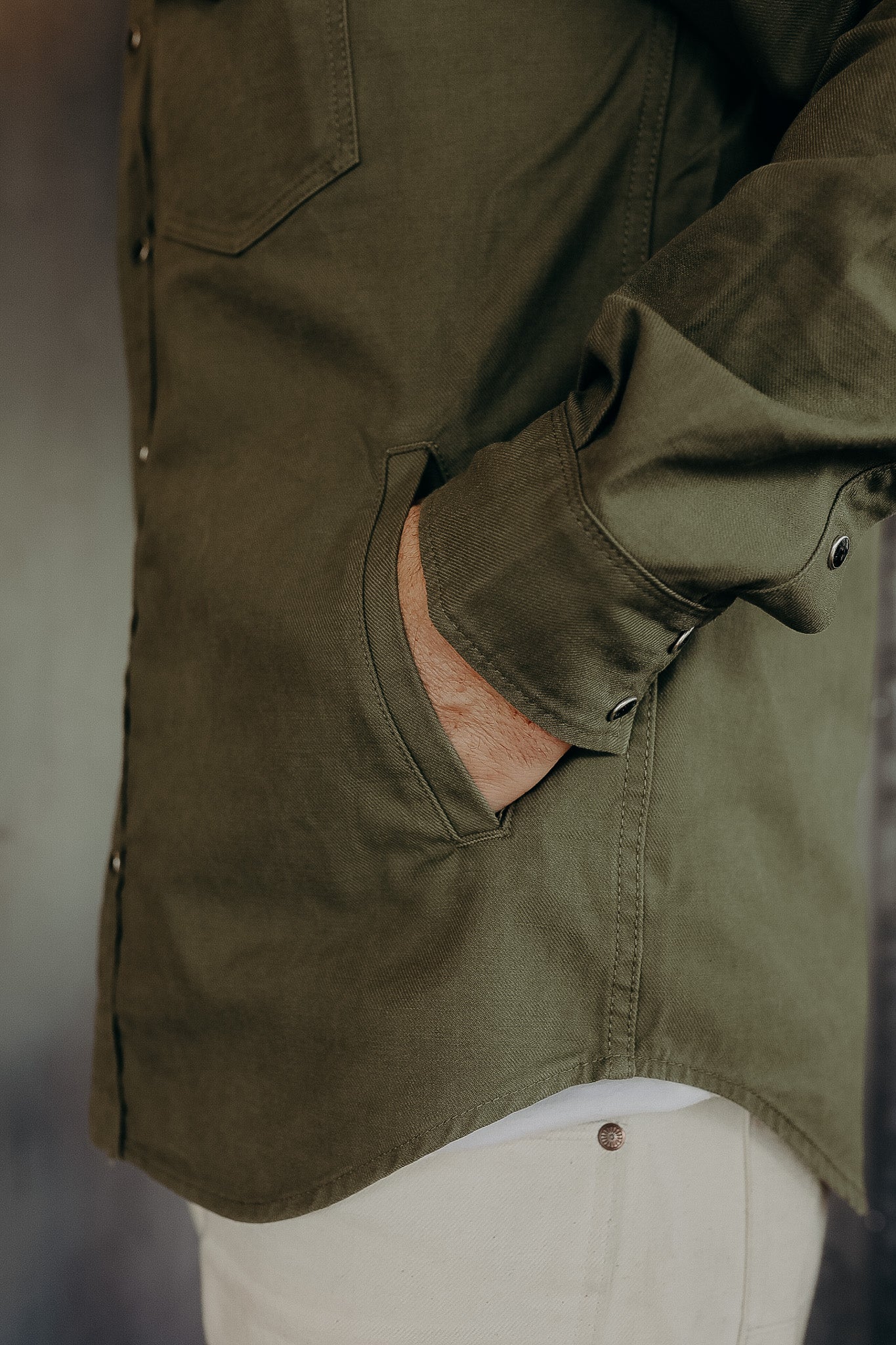 Close-up of a person wearing an olive green button-up shirt with hand in side pocket and beige pants