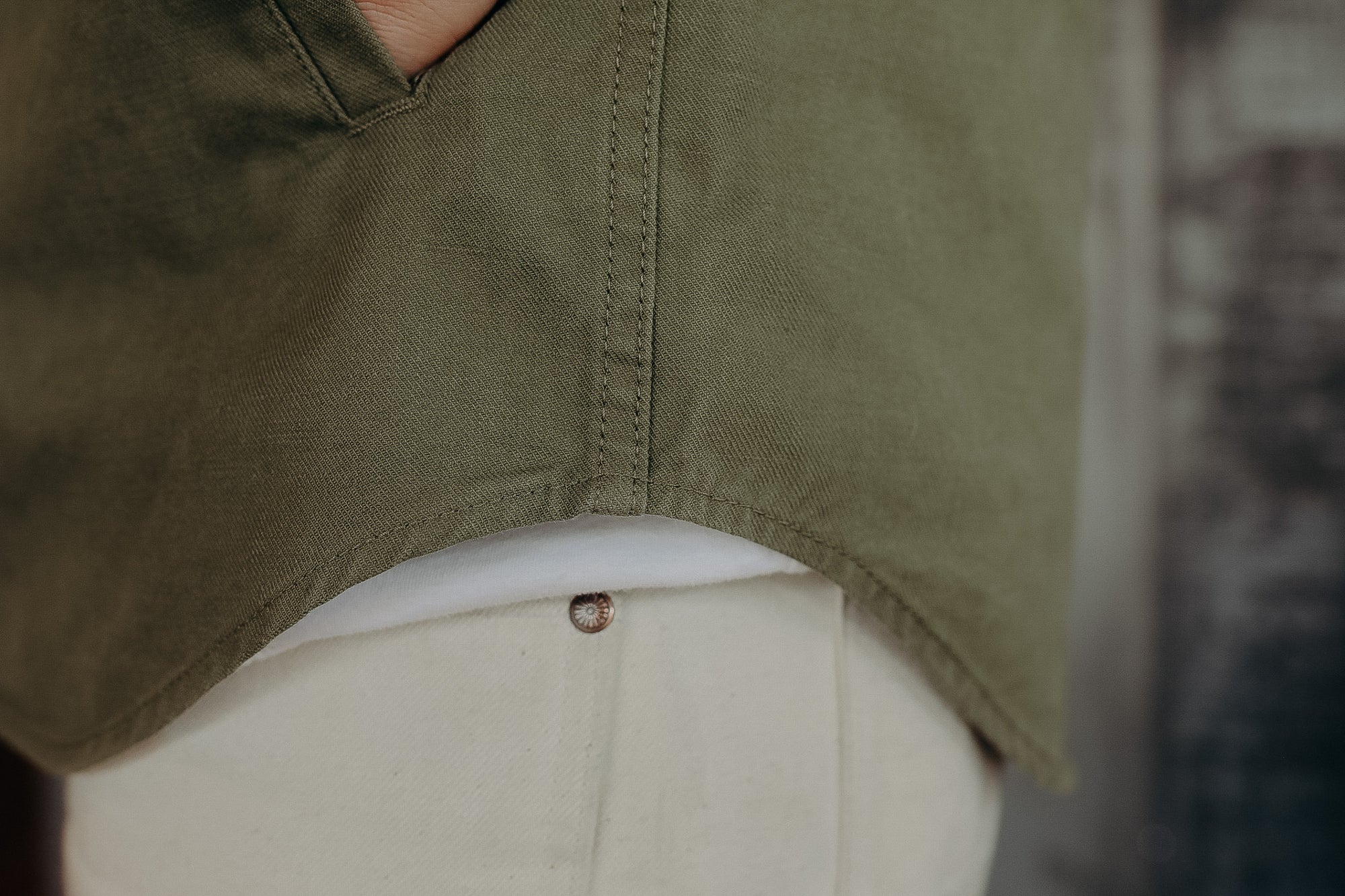 Close-up of olive green shirt hem over white fabric and light-colored pants with rivet detail
