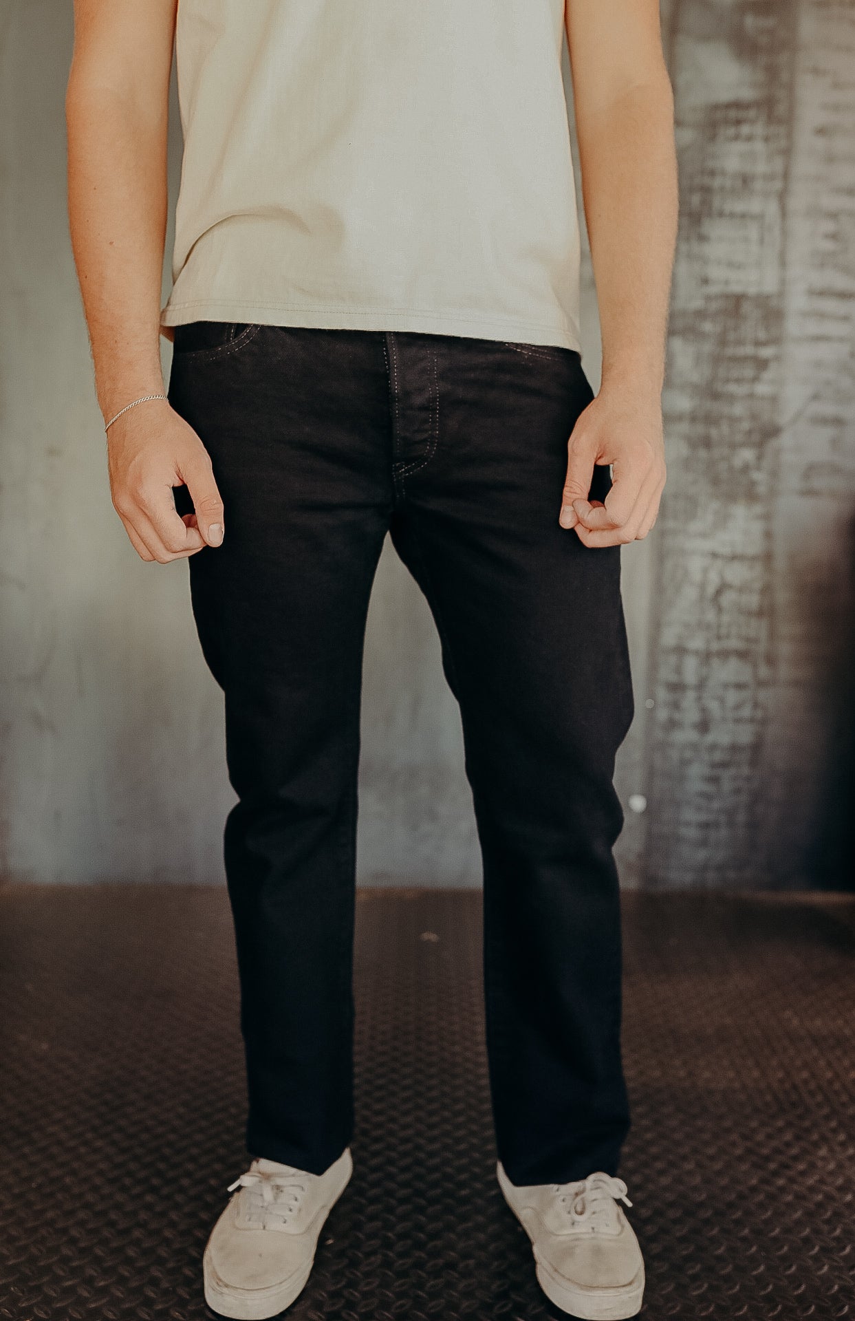 Man wearing black jeans with white sneakers and a light beige t-shirt standing on industrial metal floor