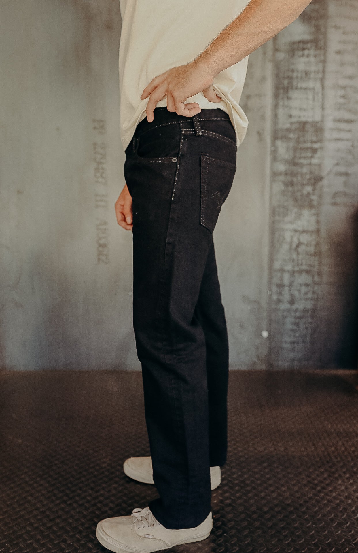 Side view of person wearing black denim jeans and white sneakers in industrial setting