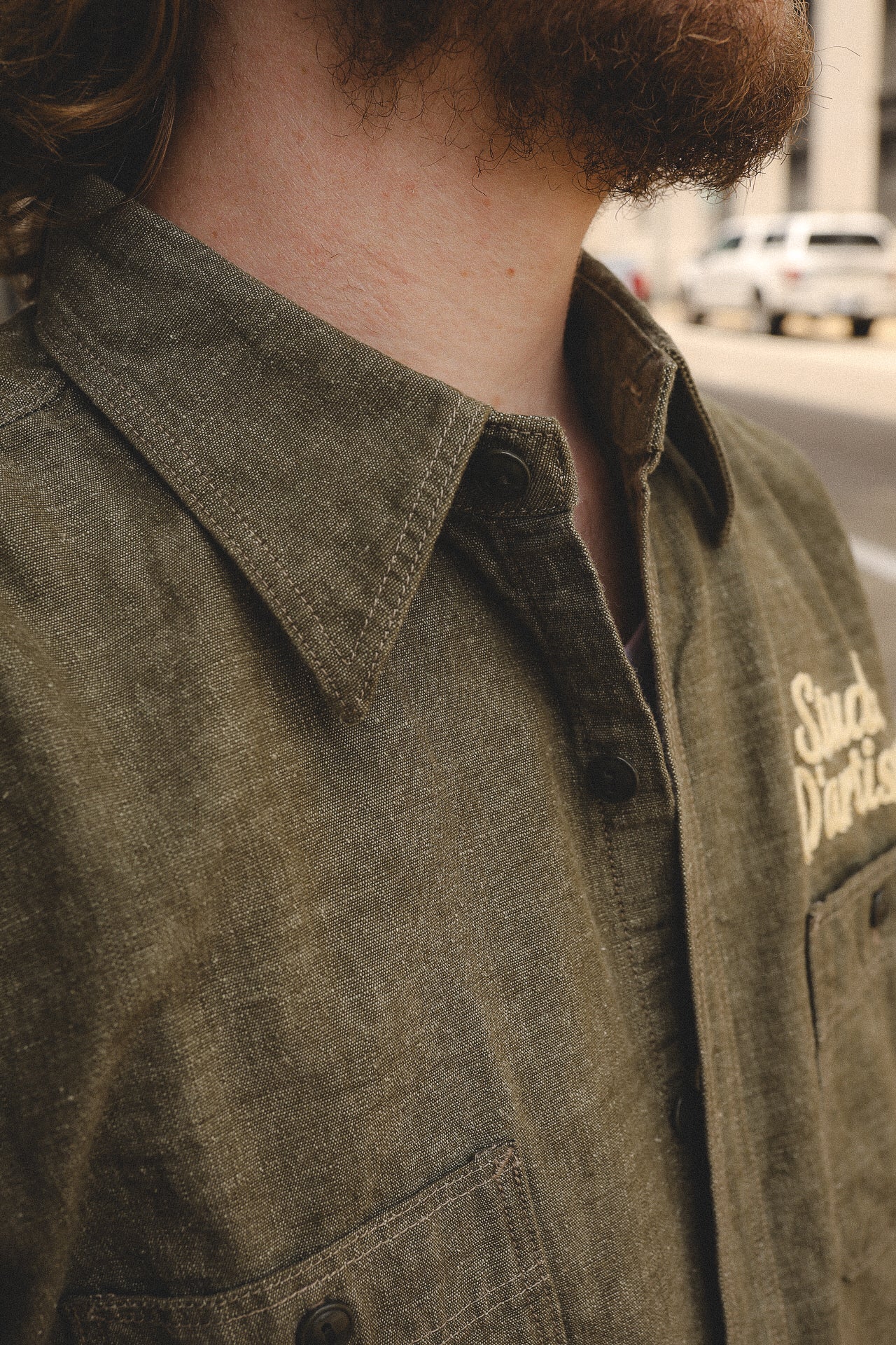 Close-up of a man wearing olive-green button-up shirt with collar and chest pocket in urban setting