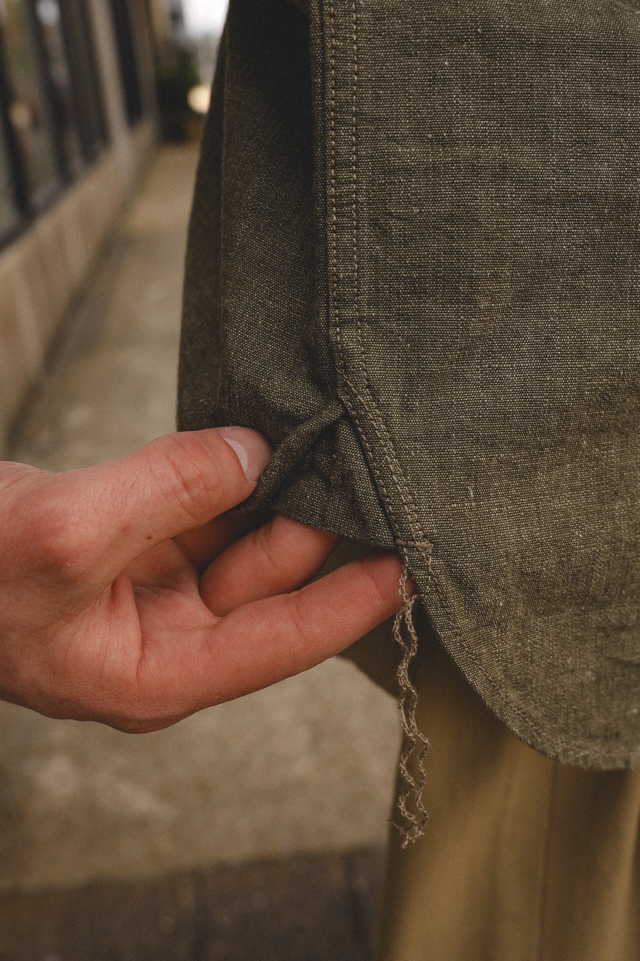 Close-up of a hand holding the frayed hem of a brown woven fabric garment outdoors