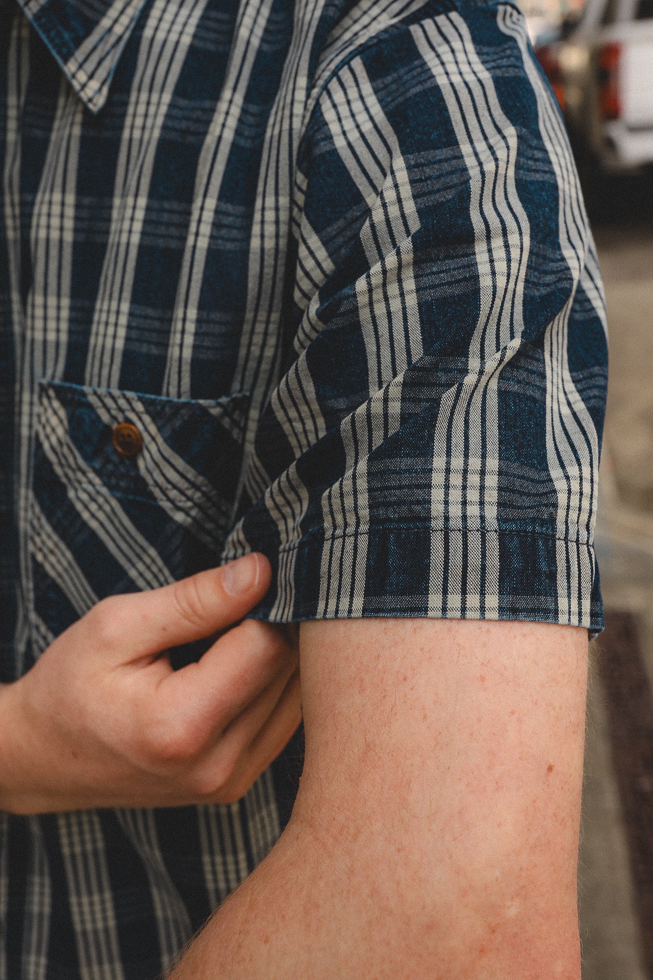 Close-up of person rolling up short sleeve on blue and white plaid shirt with button pocket