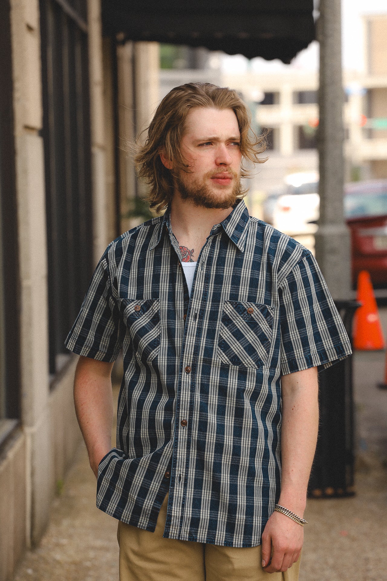 Man wearing short-sleeve blue and beige plaid button-up shirt standing on city sidewalk