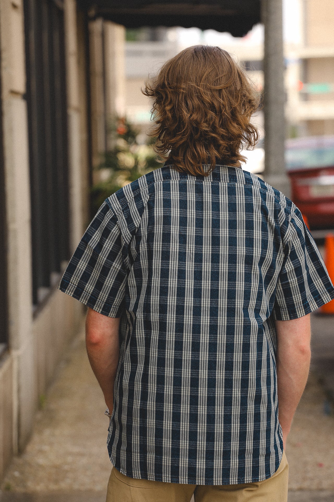 Man with medium-length brown hair wearing a blue and white striped short-sleeve shirt outdoors