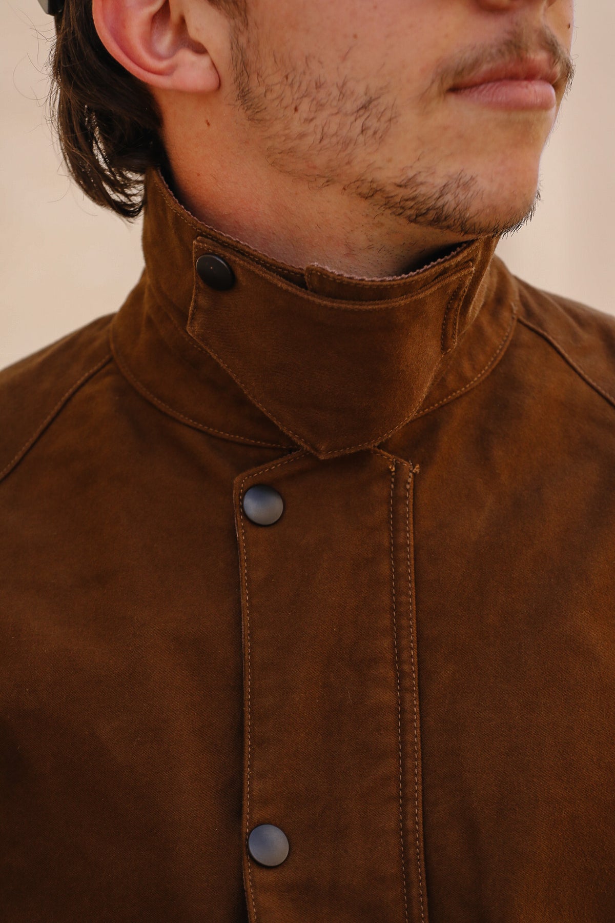 Close-up of a man wearing a brown suede or nubuck jacket with a high stand collar and snap-button front.